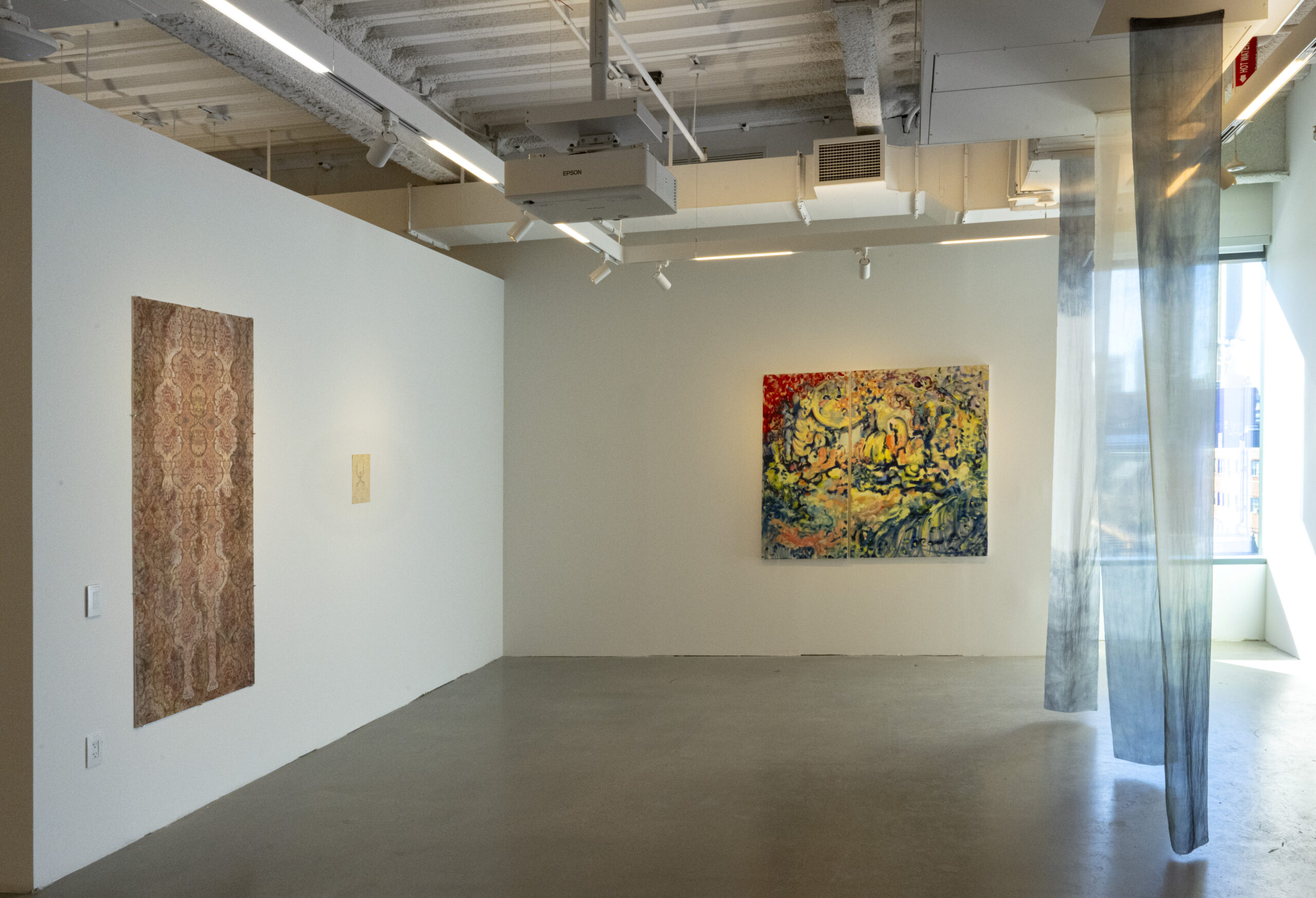 A large contemporary gallery space featuring abstract and landscape-inspired paintings. The foreground presents an orange-toned painting that appears to depict a reflection, while additional abstract works in warm and cool color palettes line the walls. A dark fabric panel is prominently displayed in the background, adding contrast and dimension to the exhibition.