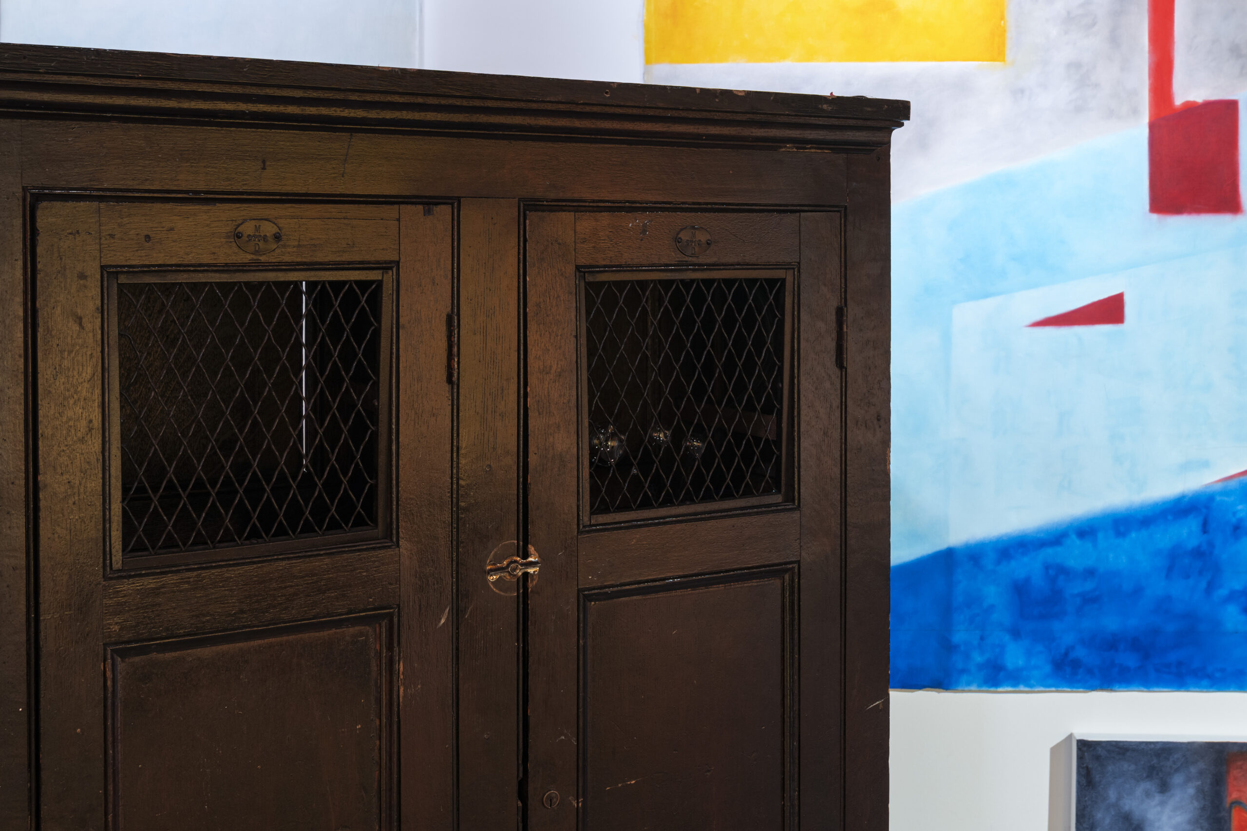 A detail shot of an installation. The top of a dark brown cabinet appears in front of shapes in yellow, light blue, and medium blue.