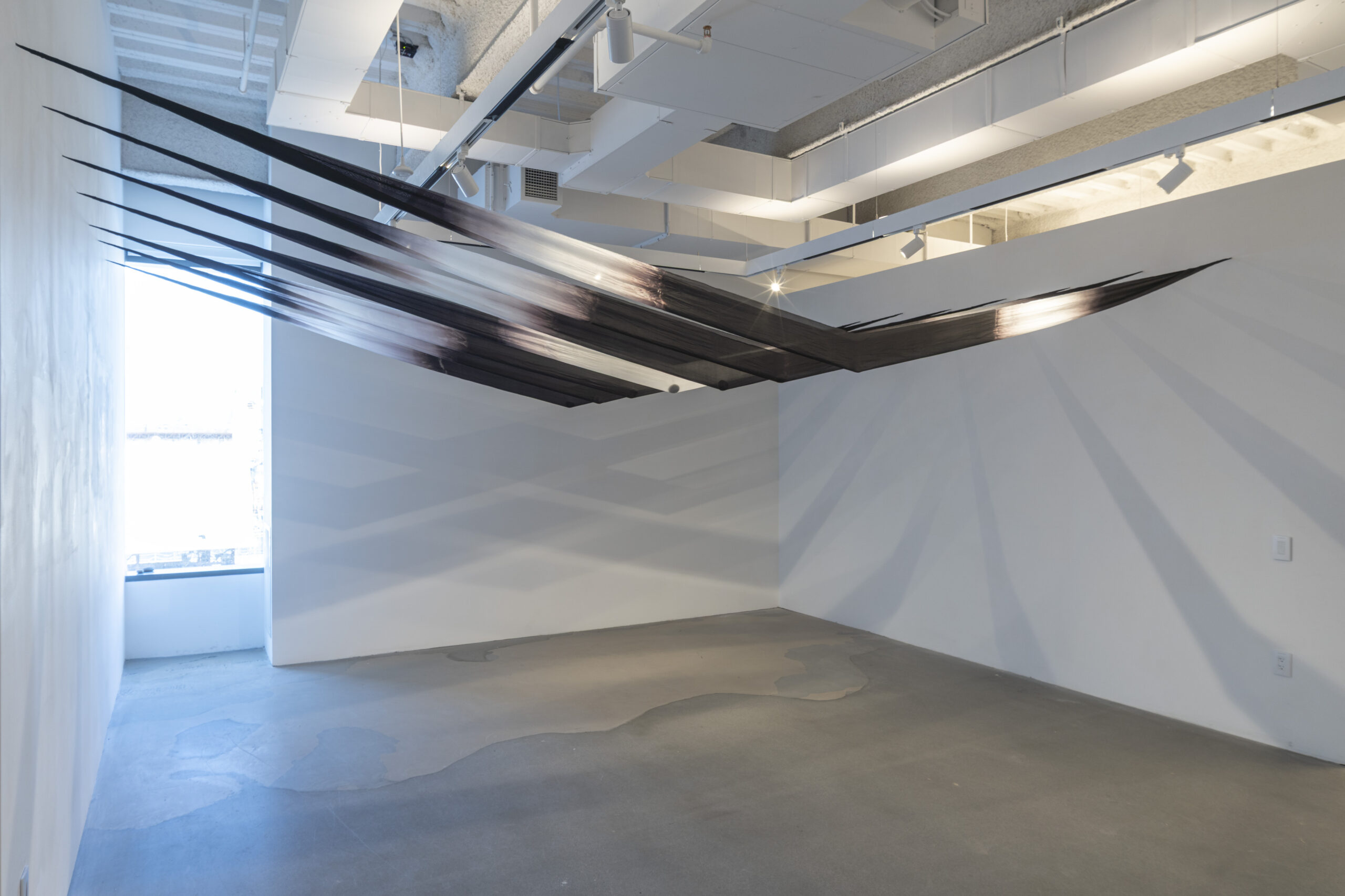 A gallery installation shot of multiple black and white V-shaped forms in a row, extending horizontally from the ceiling wall-to-wall