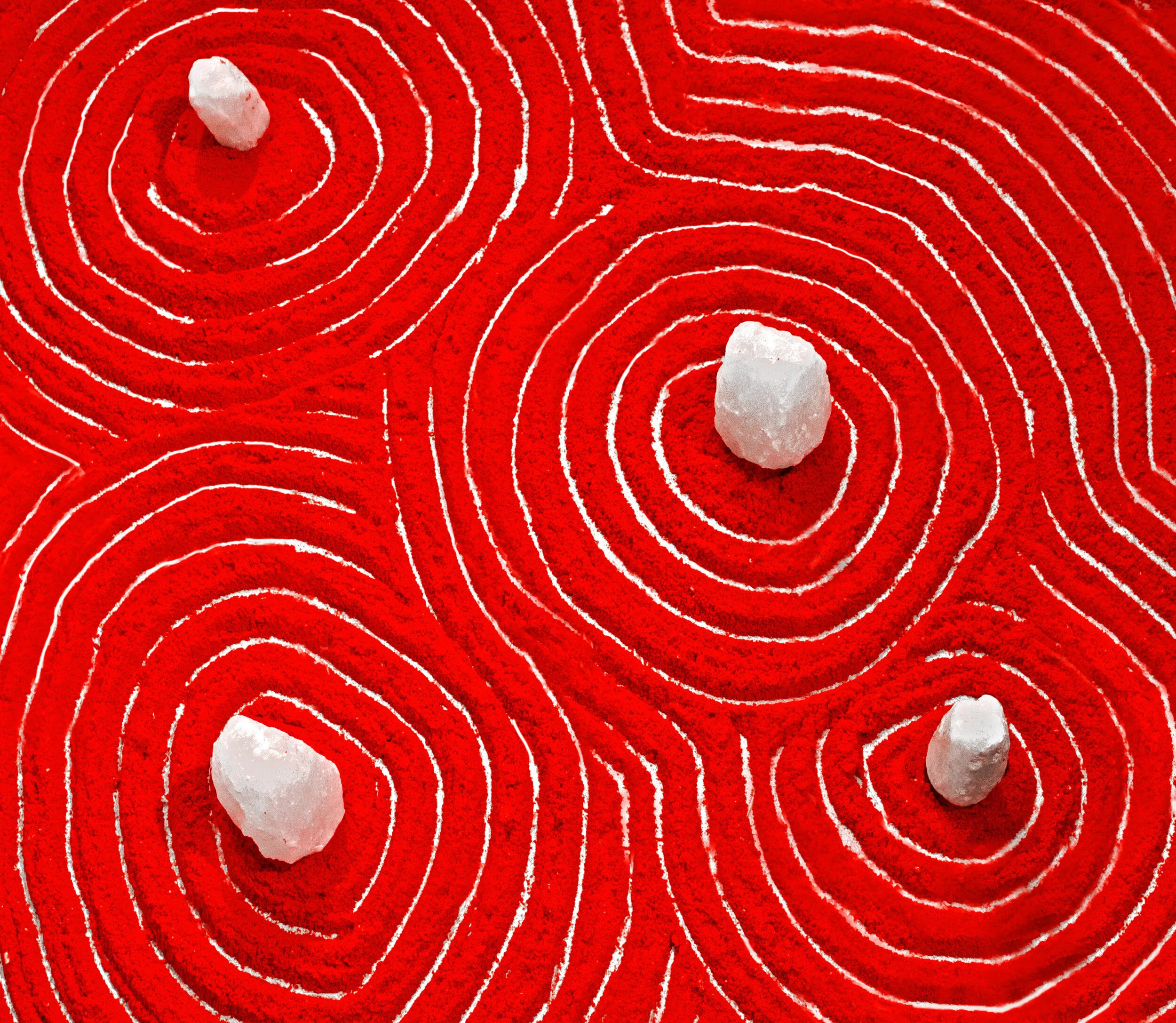 Detail image of artwork installation: powdered, bright red cheetos arranged with concentric circles raked. Crystals placed at the center of each.