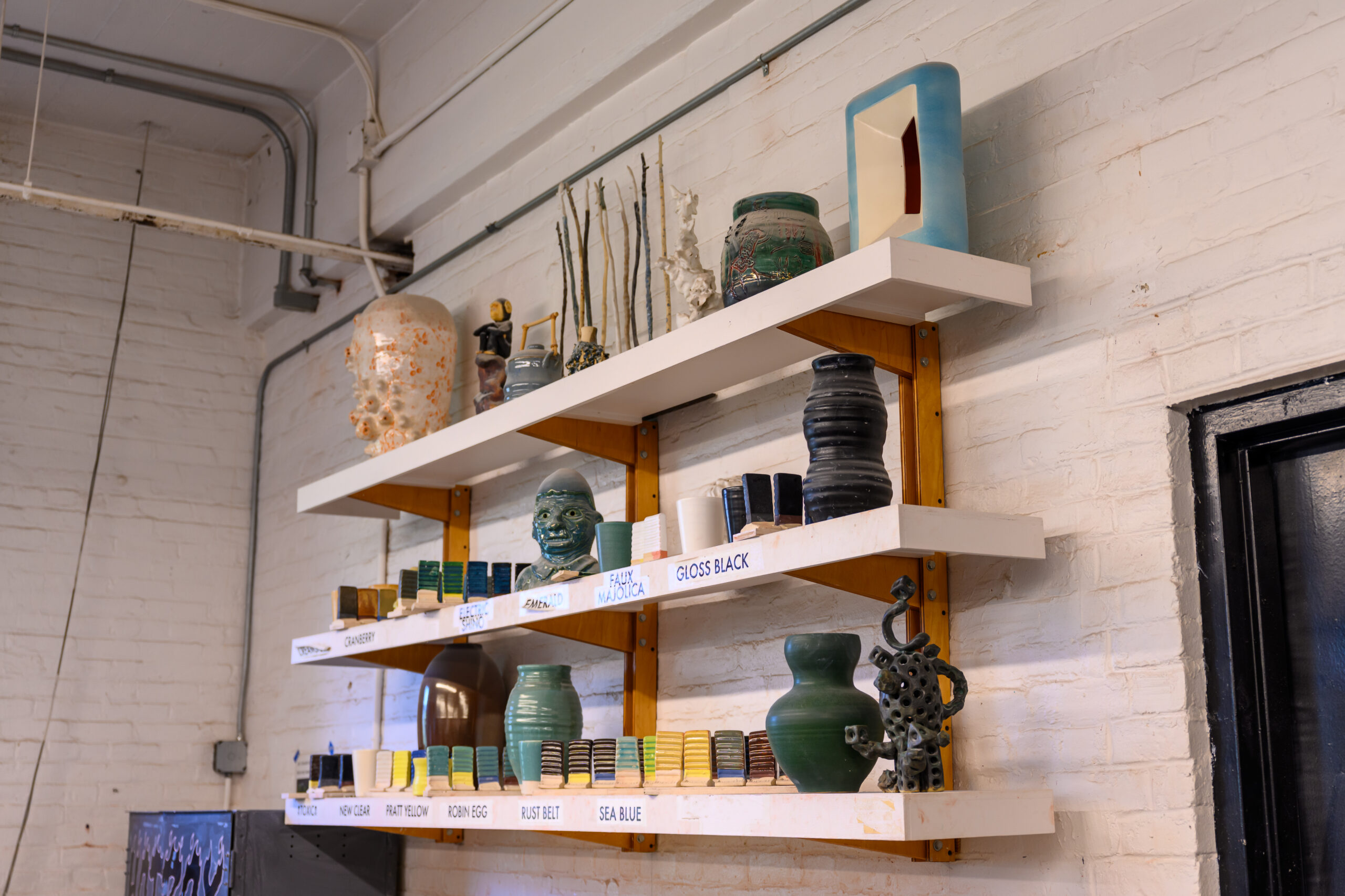 A photo of wall shelves in Fine Arts ceramics shops displaying objects with different glazes labelled