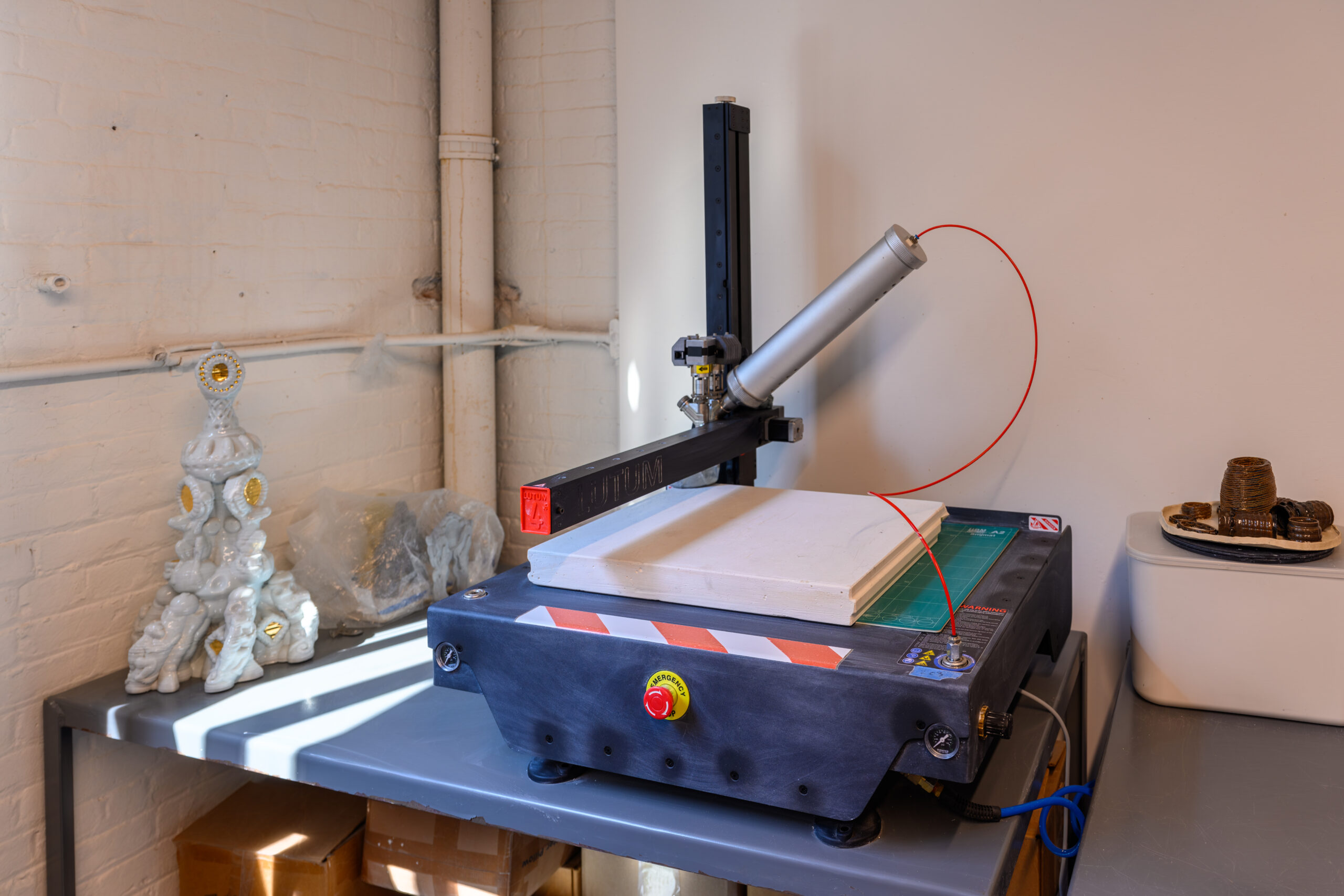 A complete, 3D-printed ceramic piece next to a 3D printer on a table in the Fine Arts ceramics shop