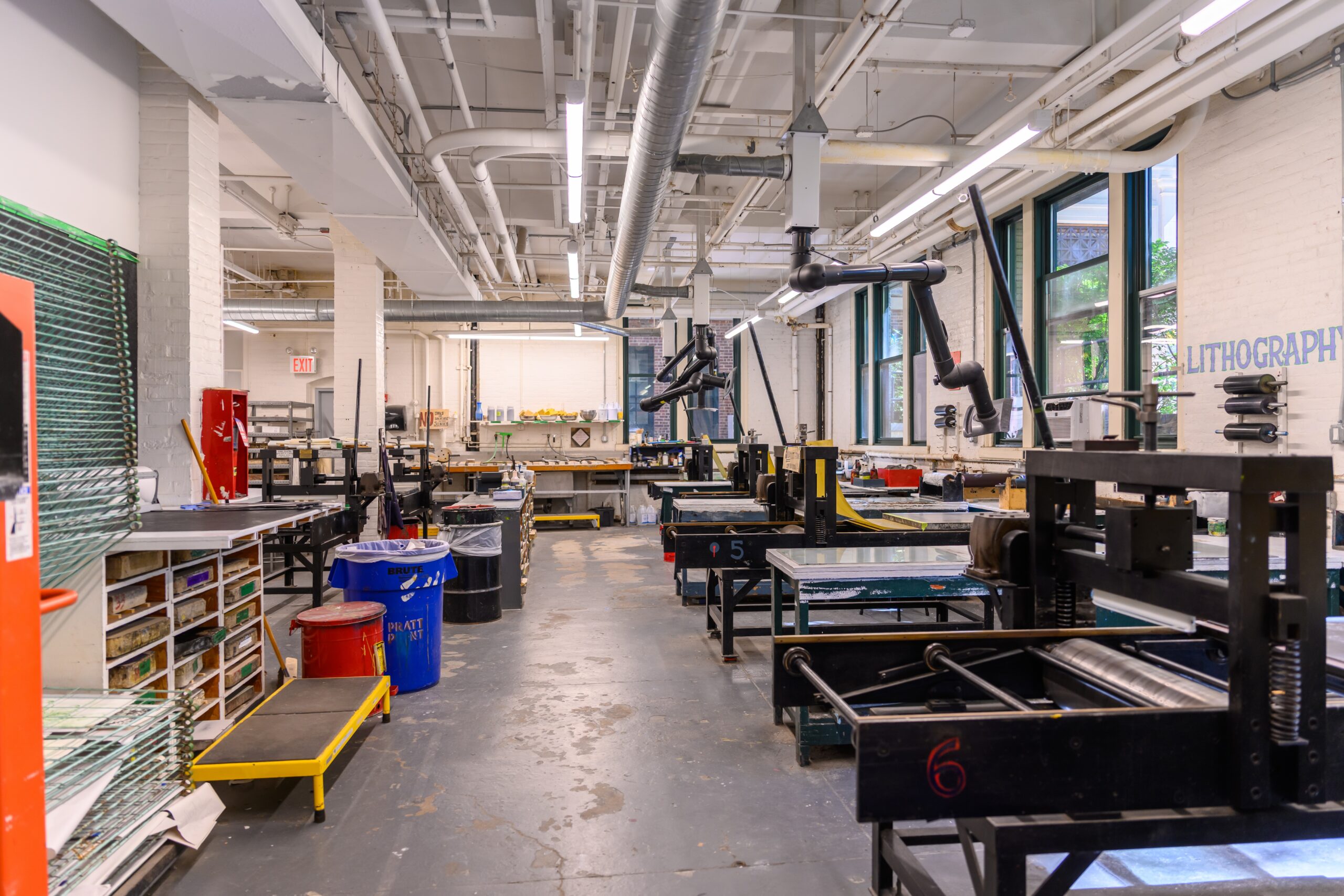 Fine Arts lithography shops, with cubbies for students' stones on the left wall and a row of presses to the right of the room, adjacent to windows.