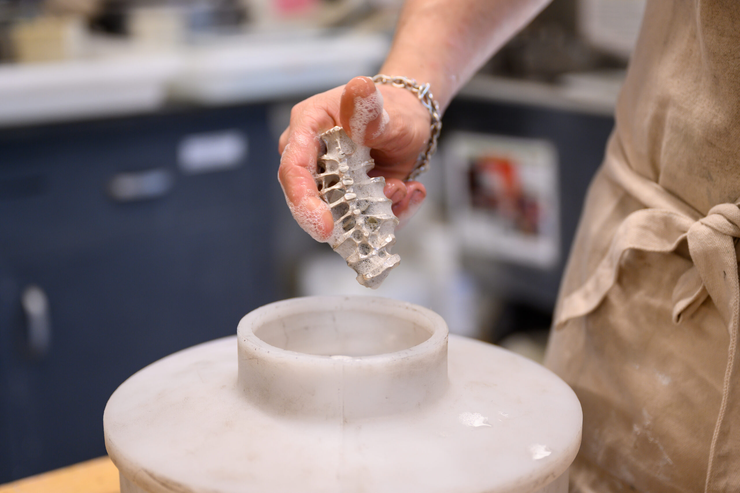 A student holds a jewelry piece in progress, covered in bubbles