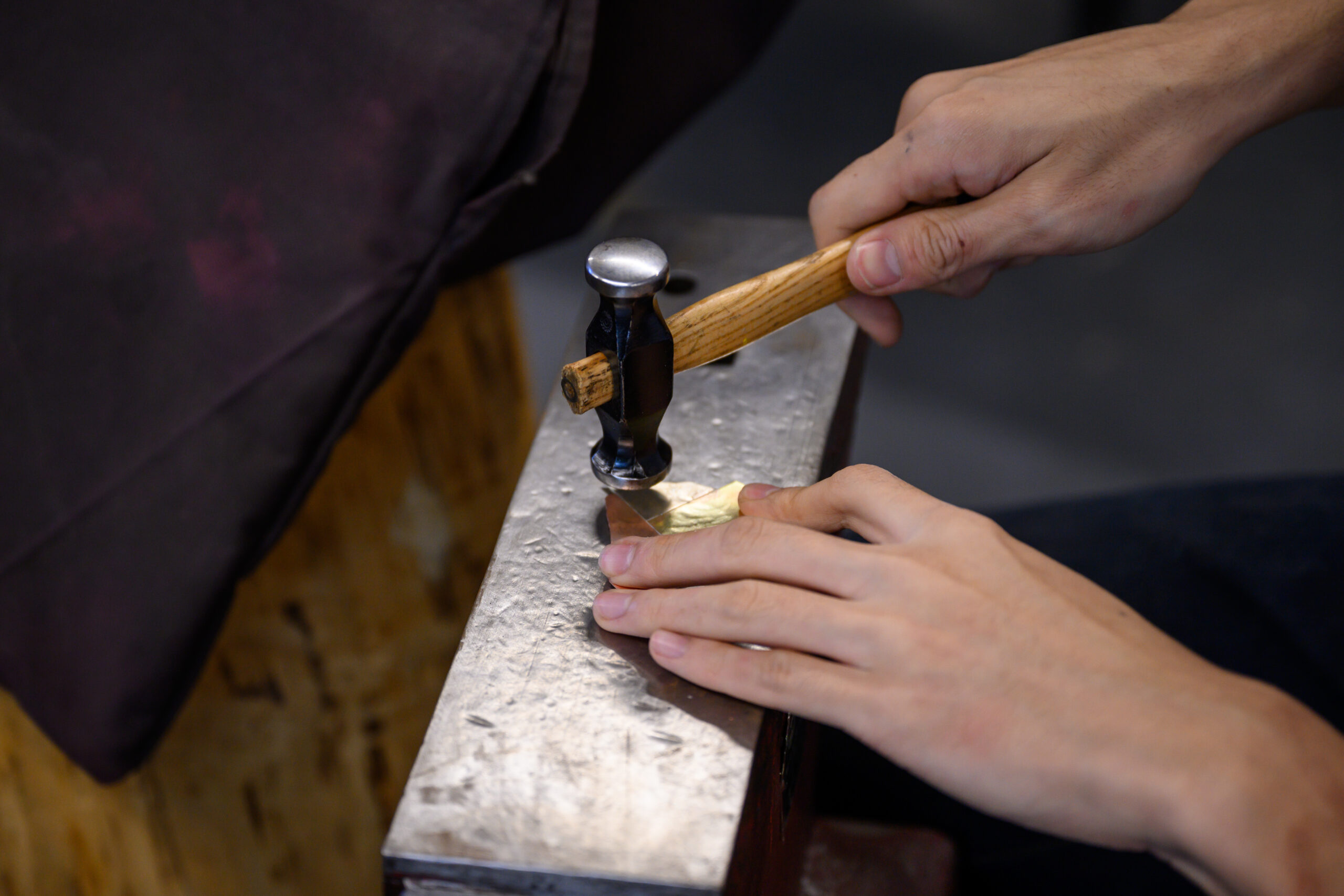 A student's hands hammering a piece of metal at their bench