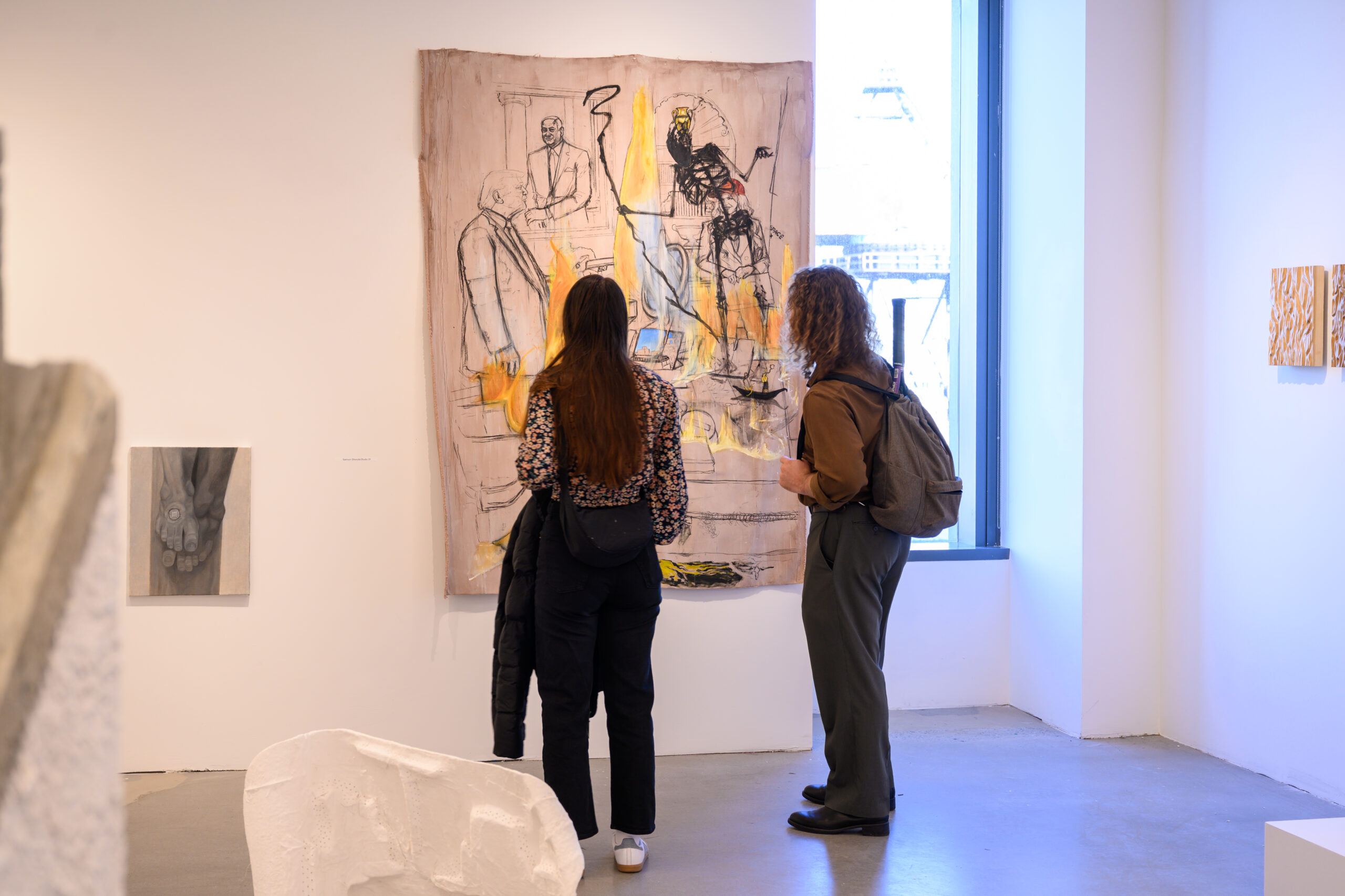 Two visitors look at a large abstract painting in a brightly-lit gallery at Dock 72. Next to the large painting is a small black and grey work. In the foreground are cropped sculptures.