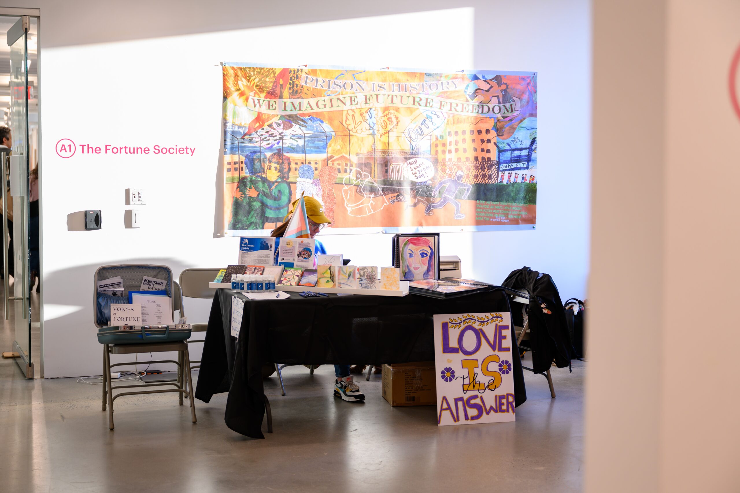 A black tableclothed table with myriad paper, pamphlets, and art are in front of a wall on which 