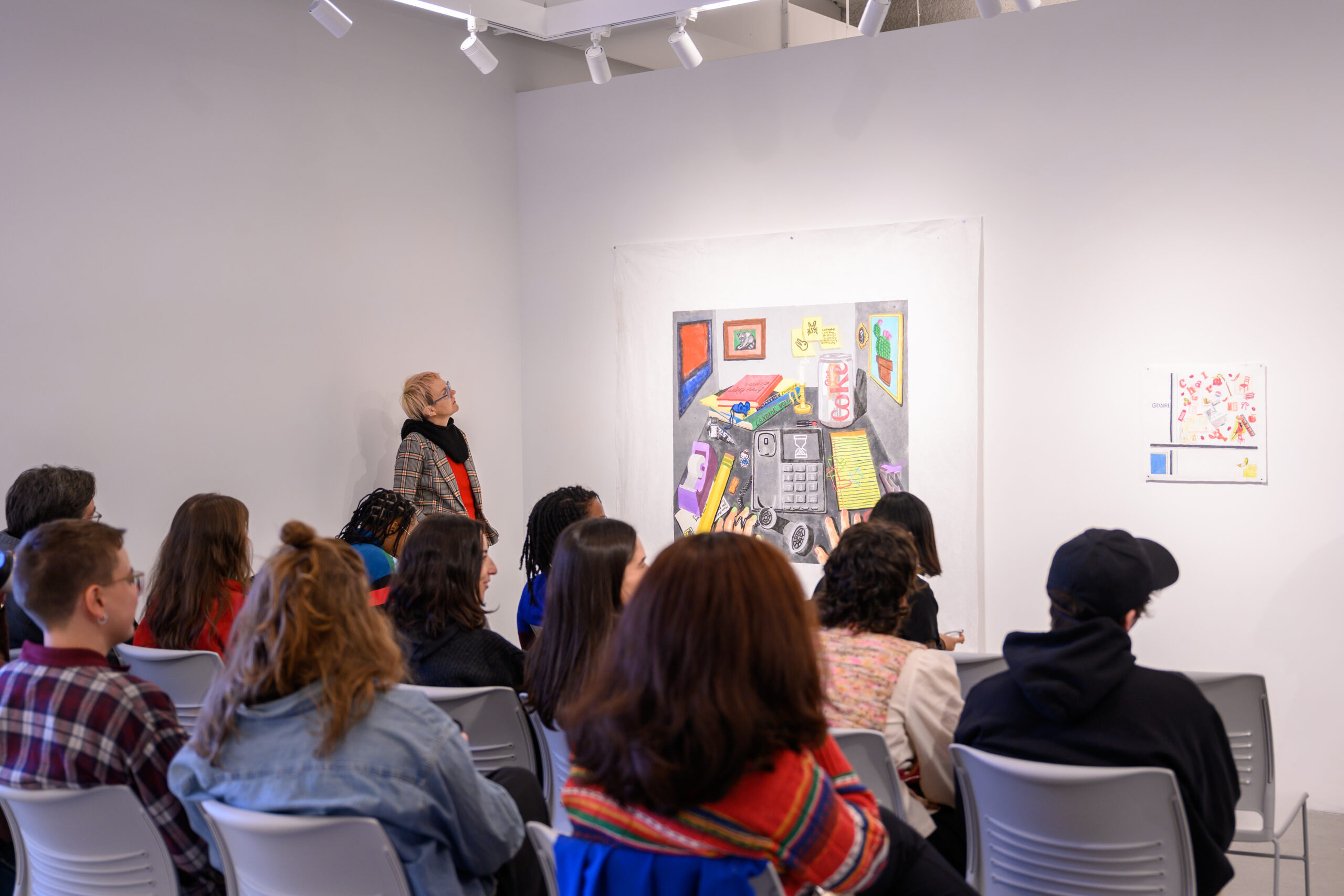 Group seated in rows in front of a wall with works installed.