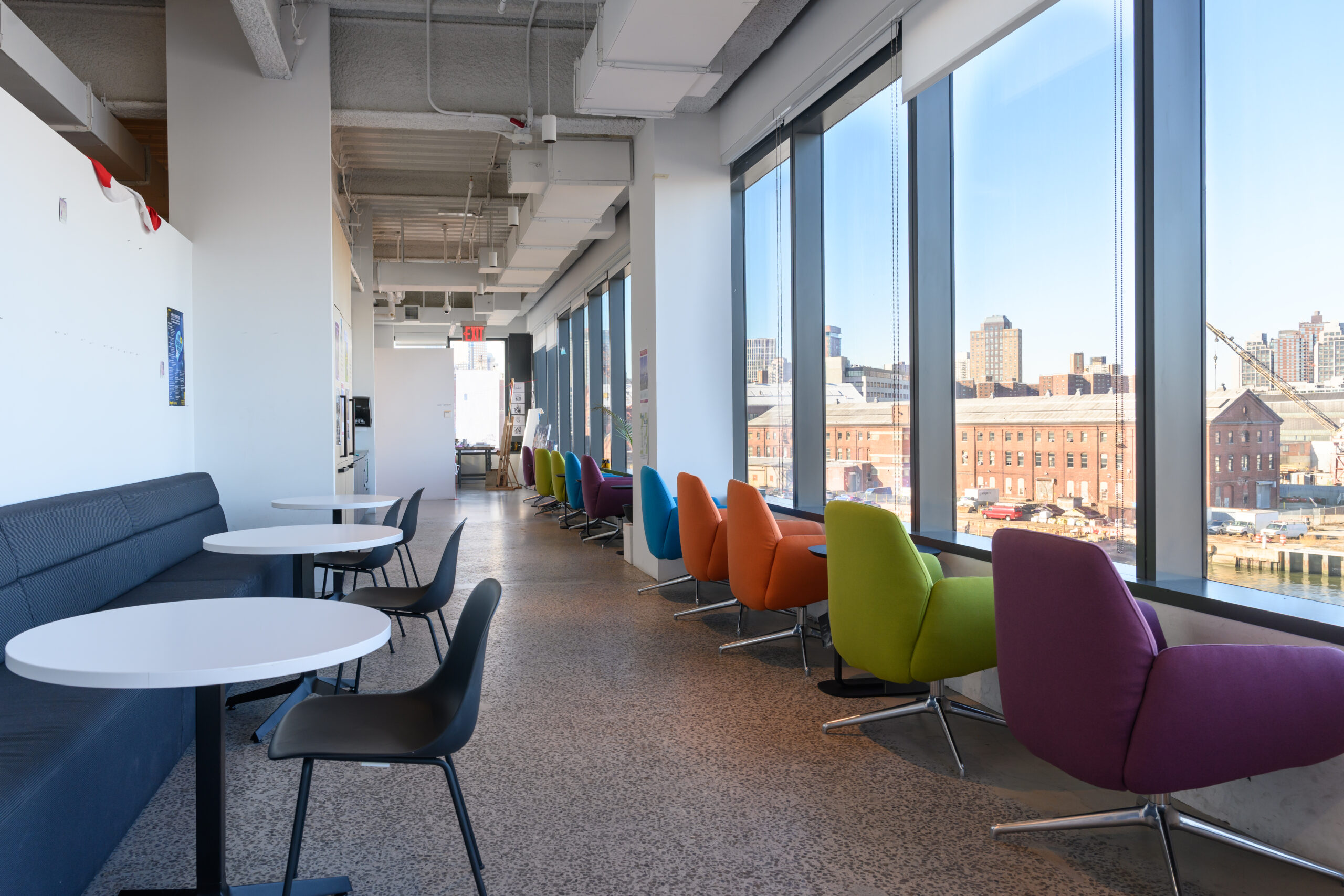 Lounge area in the Dock 72 space. A row of colorful cushioned chairs in a row facing a large window overlooking