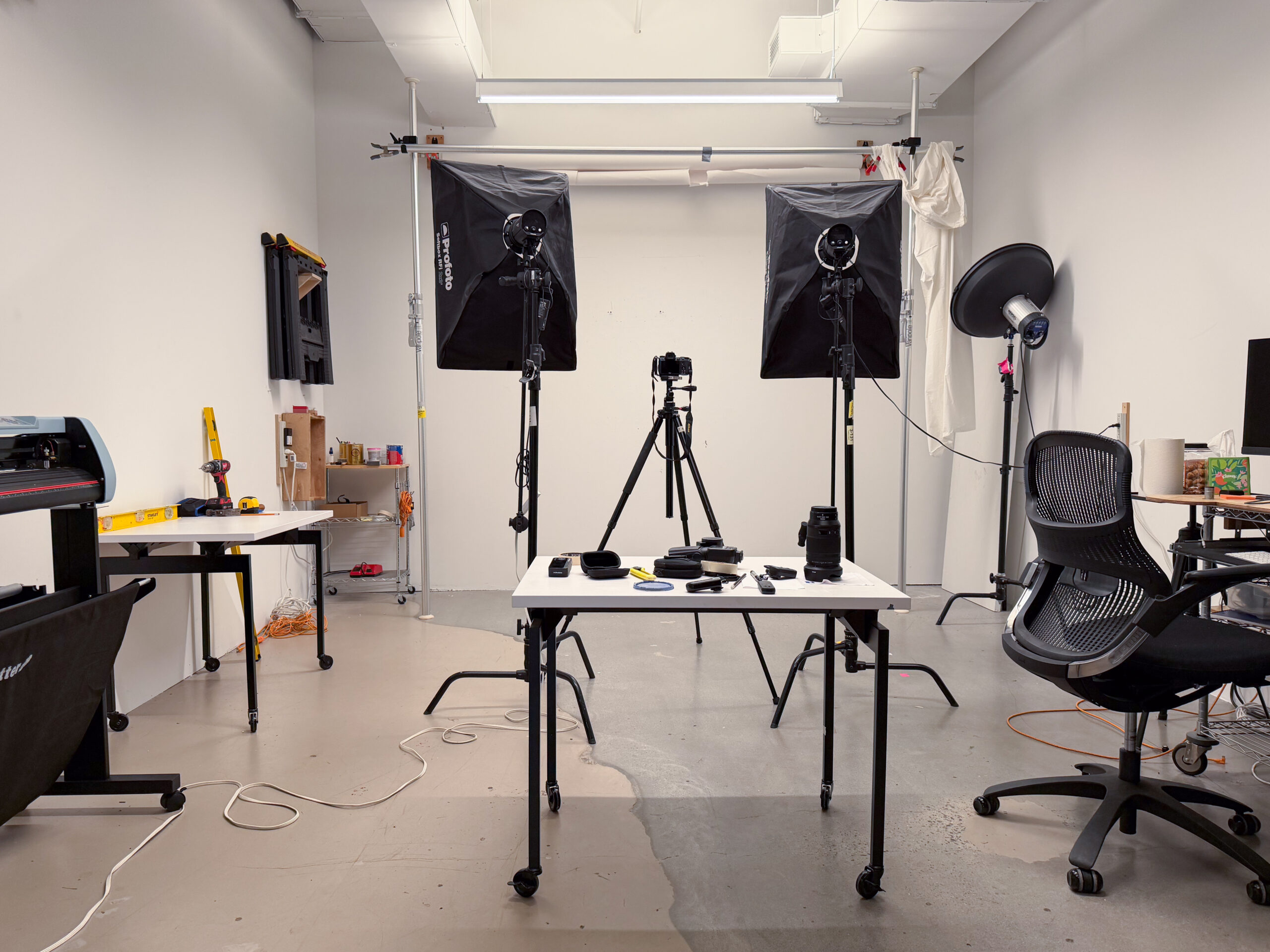 Light Lab at Dock 72 Fine Arts MFA program location. A white-walled well-lit room with a deck in the middle and set up for taking photographs with light stands, softboxes, and camera on tripod