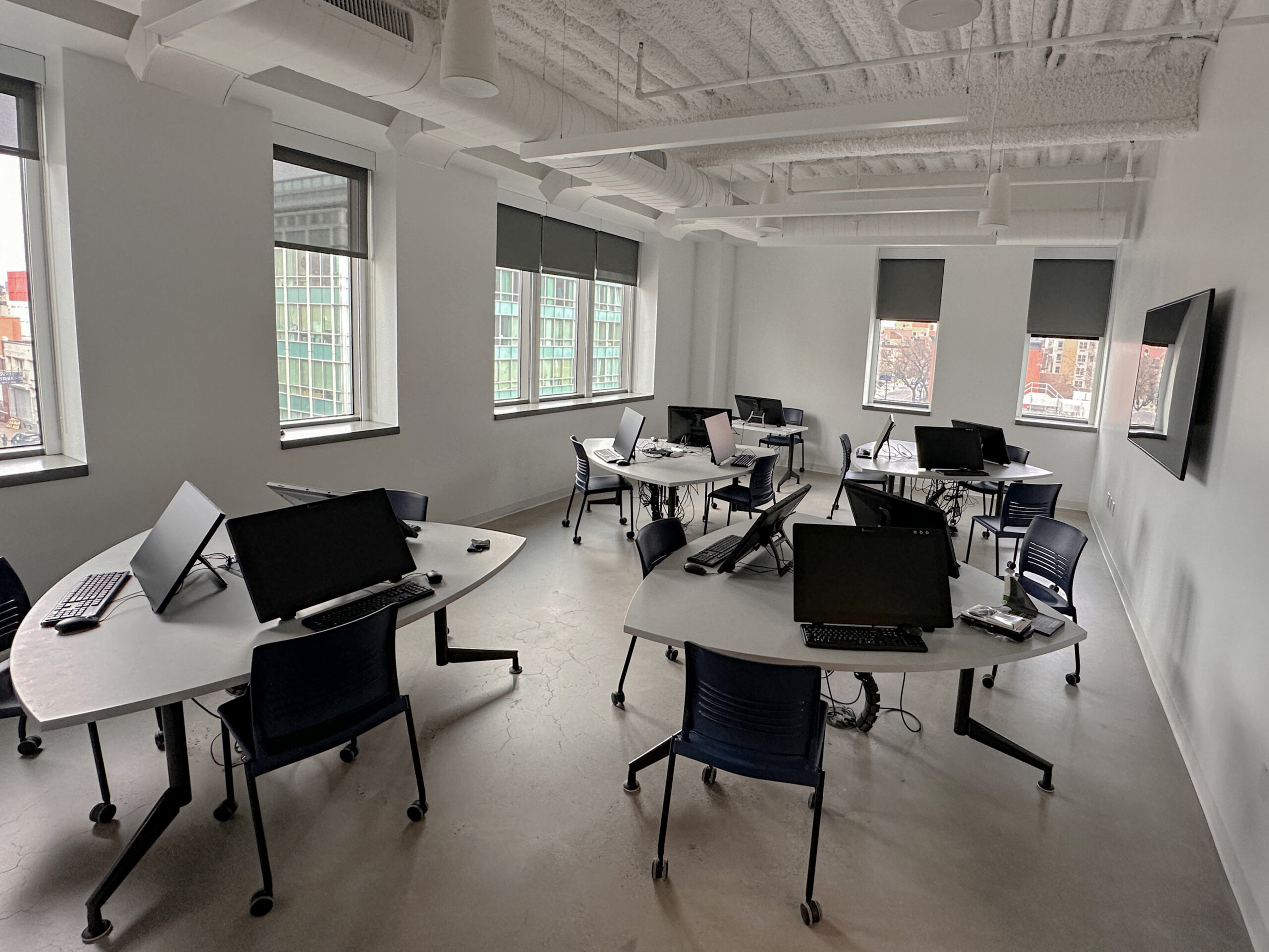 Students gather around digital drawing workstations for a critique or discussion in a storyboard and animation classroom. One student smiles while holding a stylus and speaking with classmates seated nearby, with pen displays, keyboards, and notes arranged across the desks.
