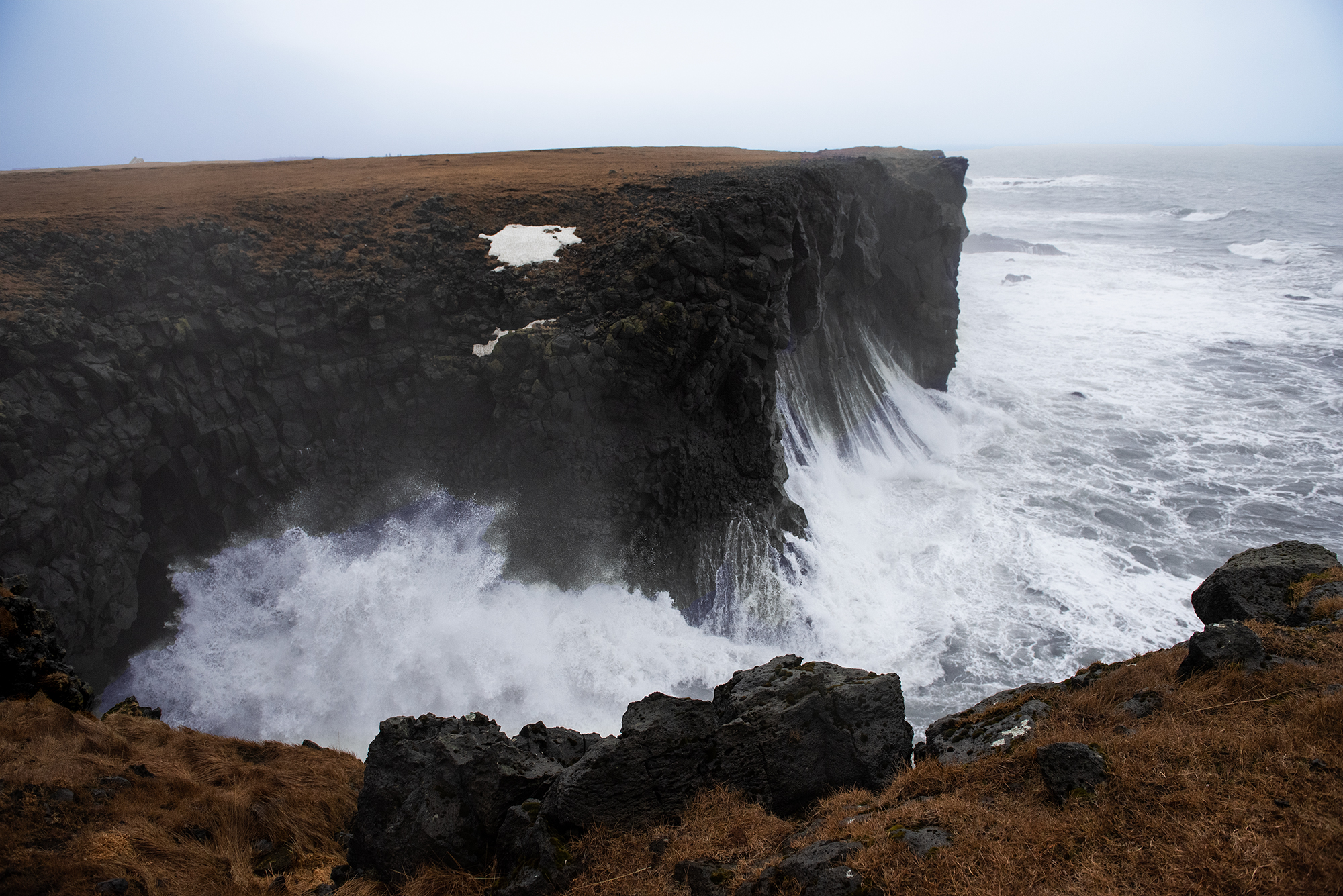 image of rock face adjecent to body of water, wave splashing on the rock