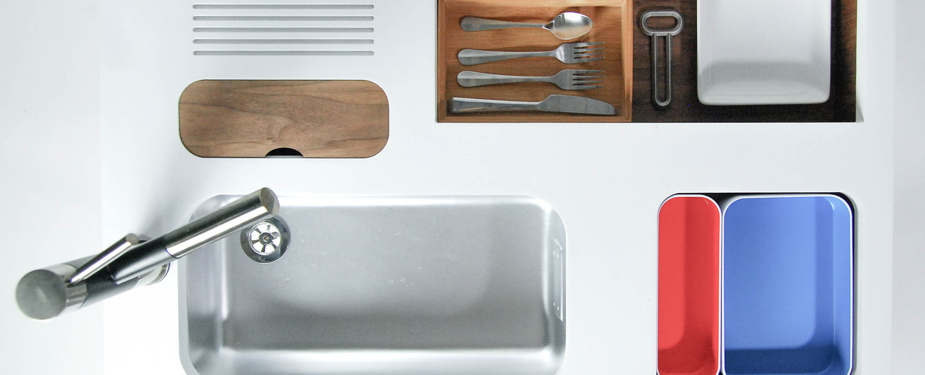 A top-down image of a kitchen counter with intricately designed storage spaces holding forks, plates and a sink