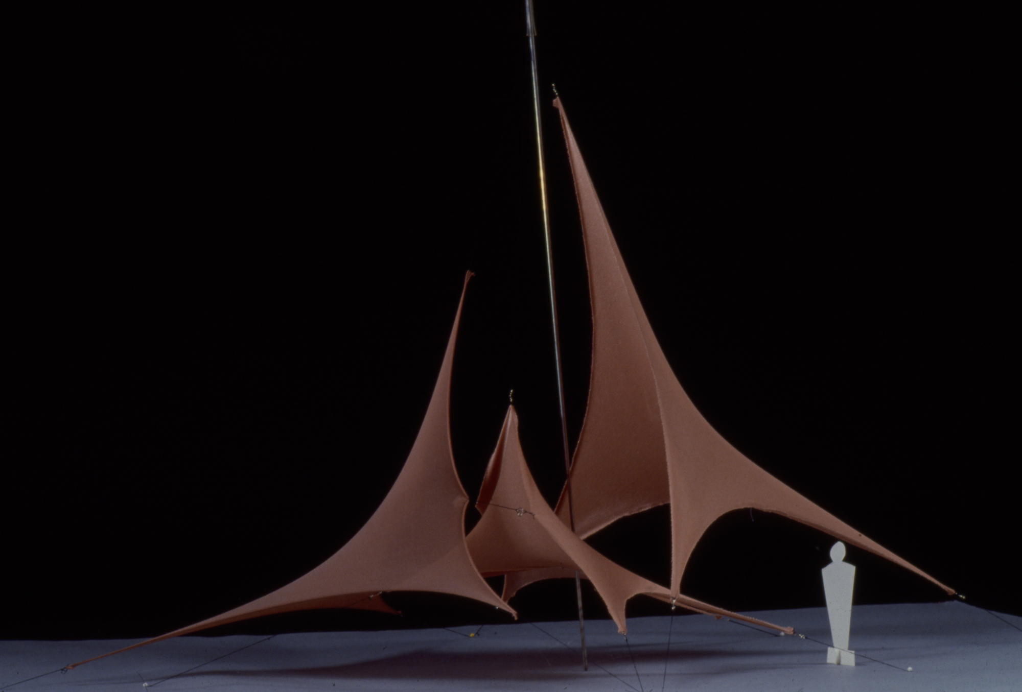 a scale model of a brown stretched canvas structure with three points and a small figure for scale