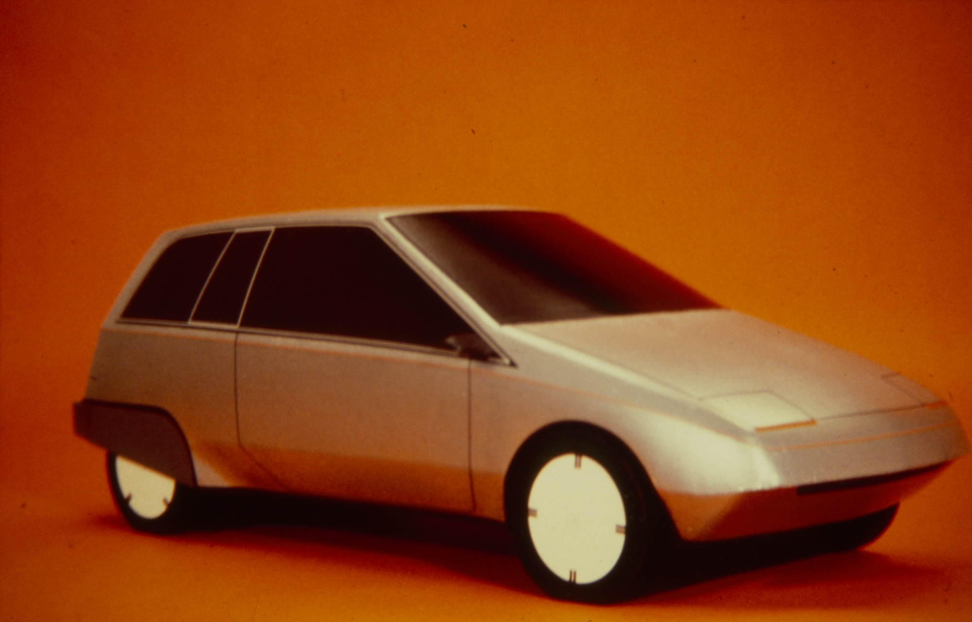 a model of a silver hatchback car on an orange backdrop