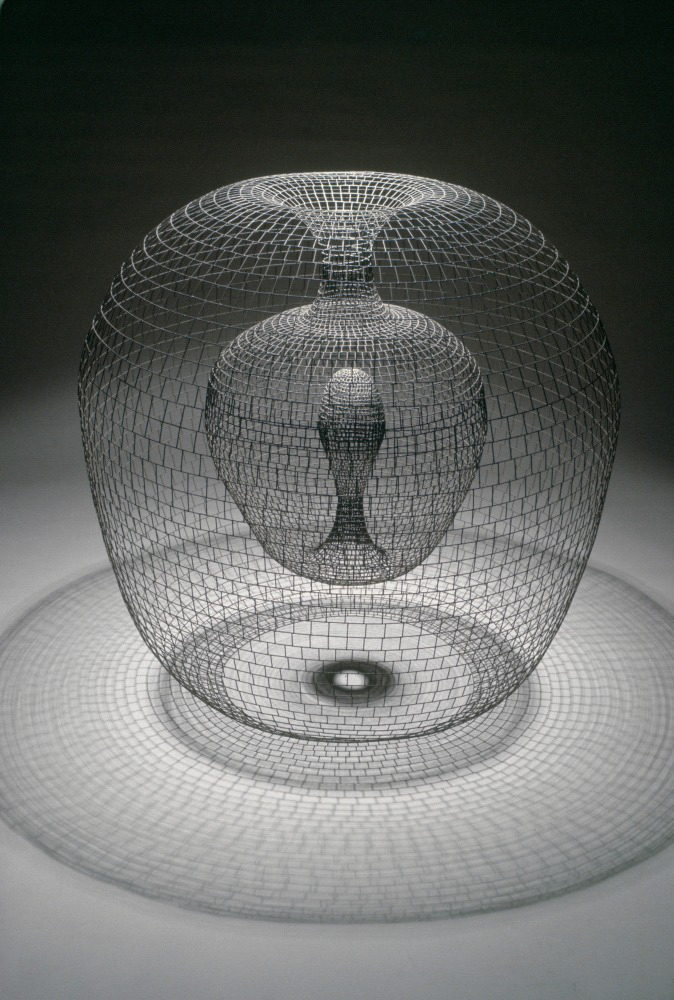 an apple-shaped form made of gridded wire which folds in on itself at the top, repeating its form in a smaller size on the interior, before then folding back into itself in the form of an upward droplet at the core