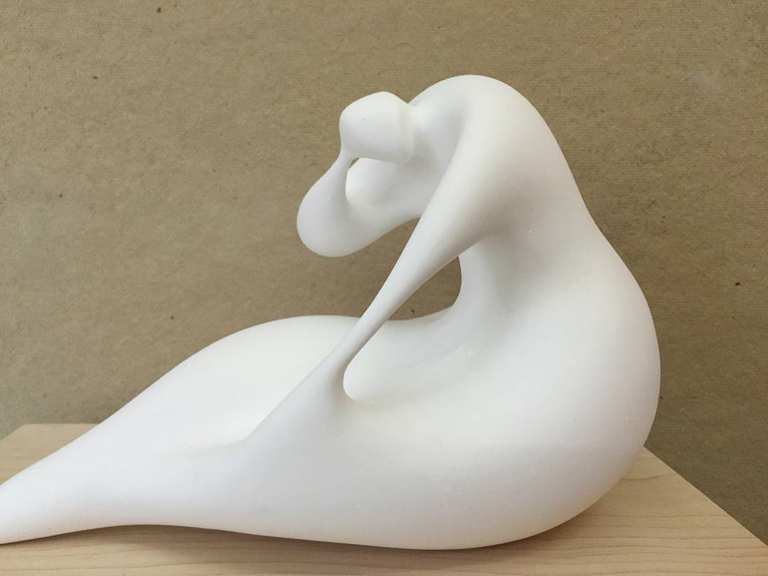 an abstract figurative sculpture made of white clay that resembles a reclining person touching their head and knee