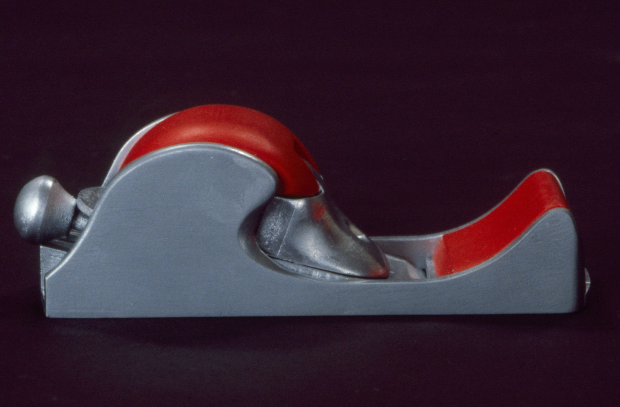 a gray metal hand plane with a red plastic handle