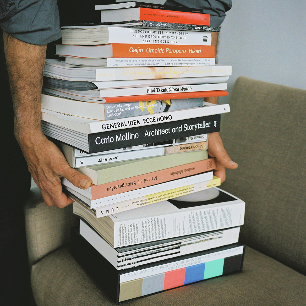 A man's hands appearing to be lifting a stack of books off of a sofa.