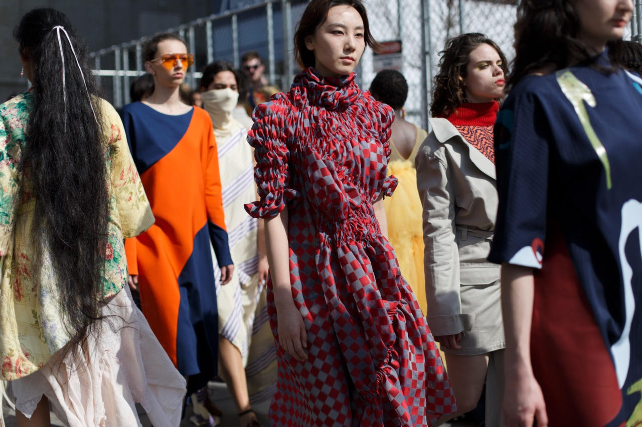 multiple models, standing in a large industrial room, at a perspective of 2 feet away, with models wearing designs from students