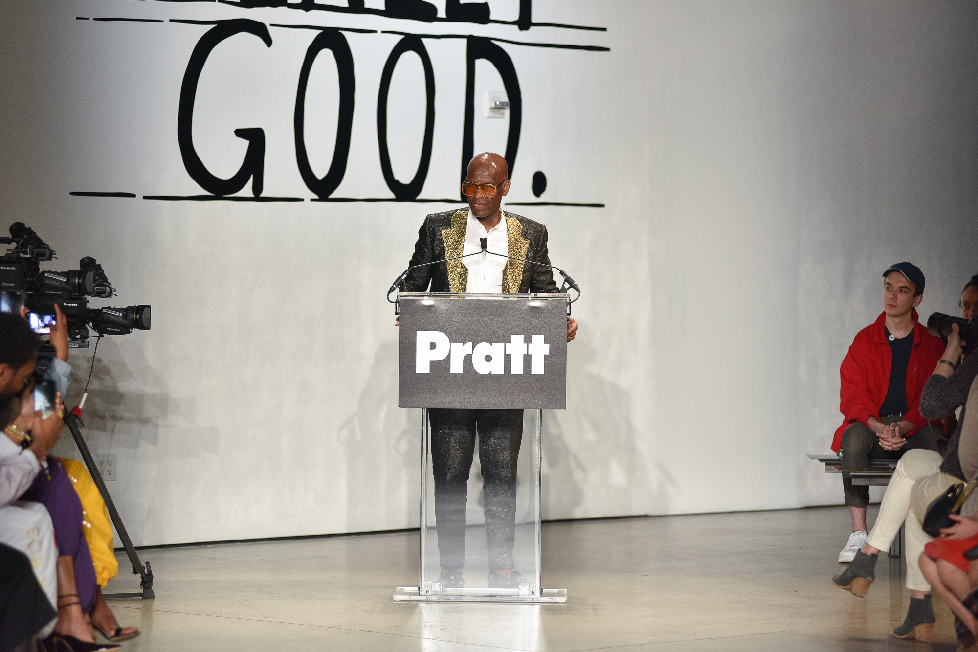 Dapper Dan standing at a podium, addressing pratt community, with rows of people seated on either side of him