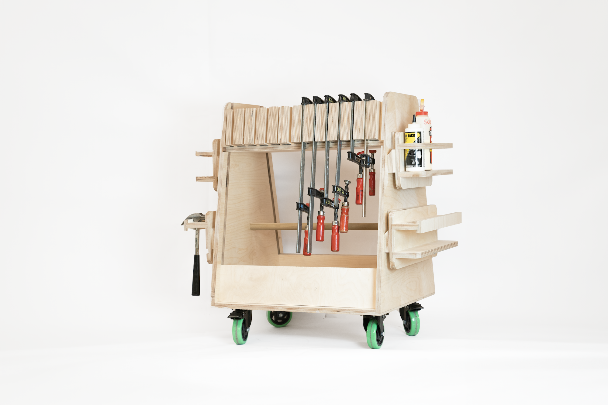 A wooden workshop cart with multiple compartments and tools organized on it. The cart features several clamps with red handles attached to the top. There are also spaces for bottles of glue and other materials on the side. The cart stands on green wheels, allowing for easy mobility. The background is plain white, emphasizing the cart's details.