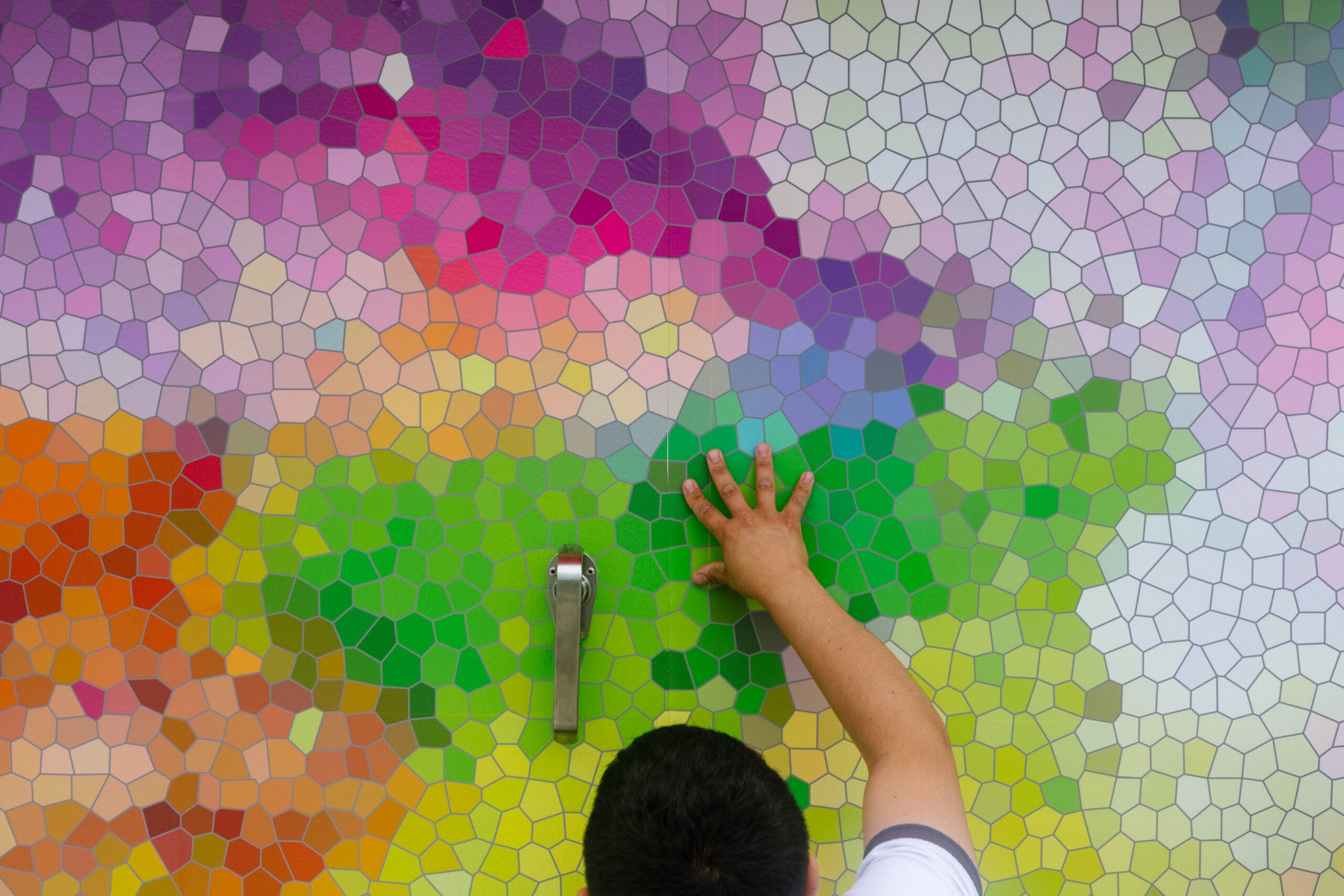 A student places their hand on a large surface covered by a brightly-colored mosaic of tiles.