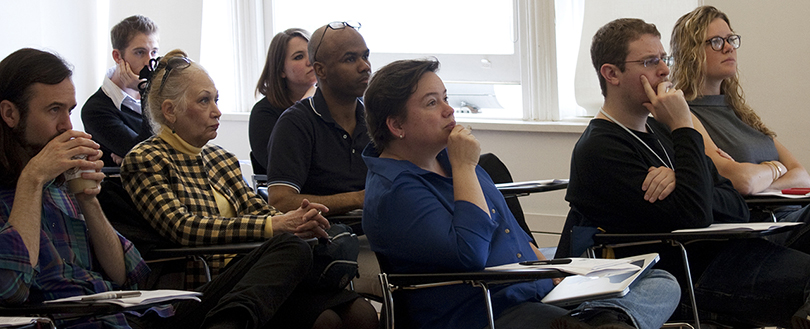 A group of student listens attentively as they look forward to the front of a classroom. The teacher is out of view.