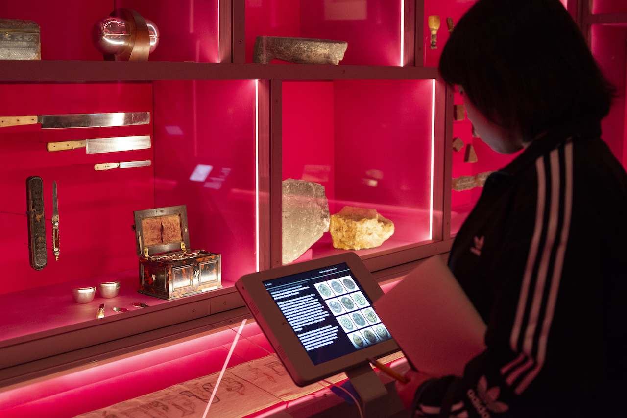 student in museum, reading from information tablet, looking at exhibit