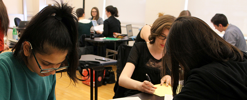 Students working in a classroom are seated at tables focusing on their work