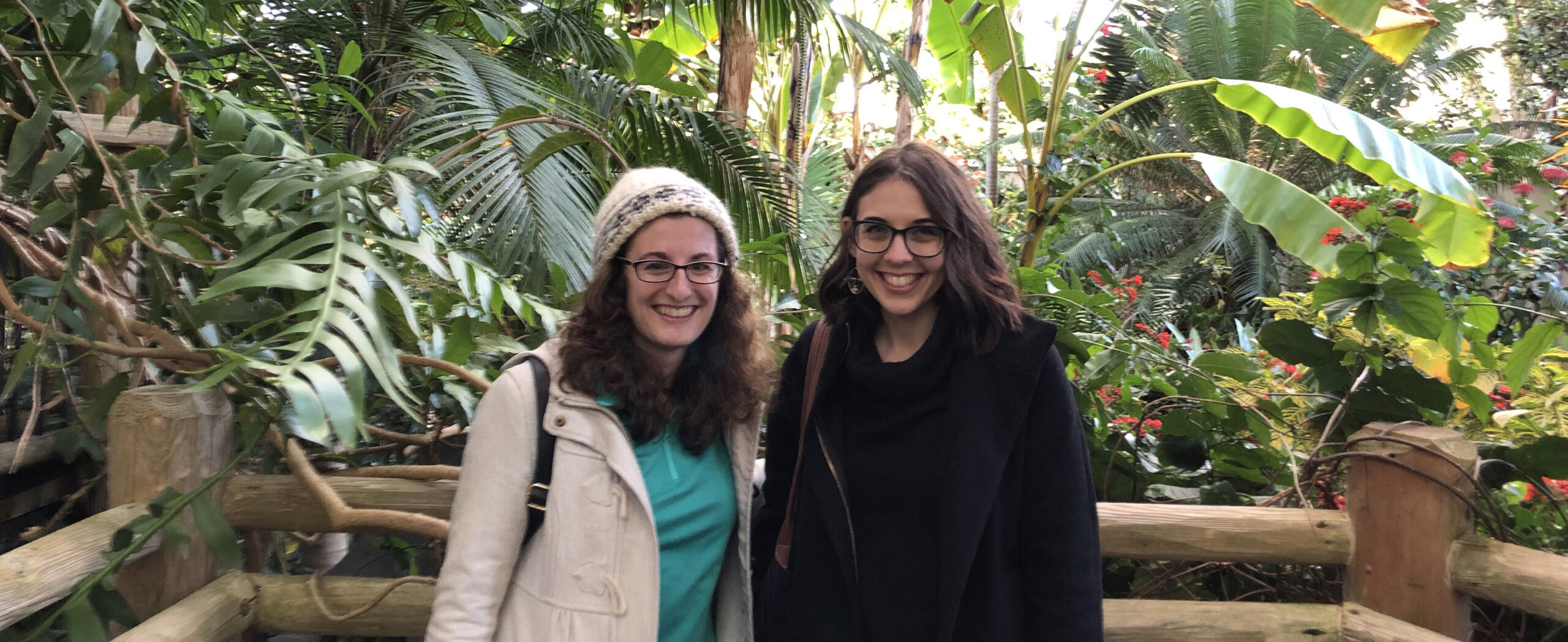 Two women standing in front of lush tropical vegetation smiling at the camera.