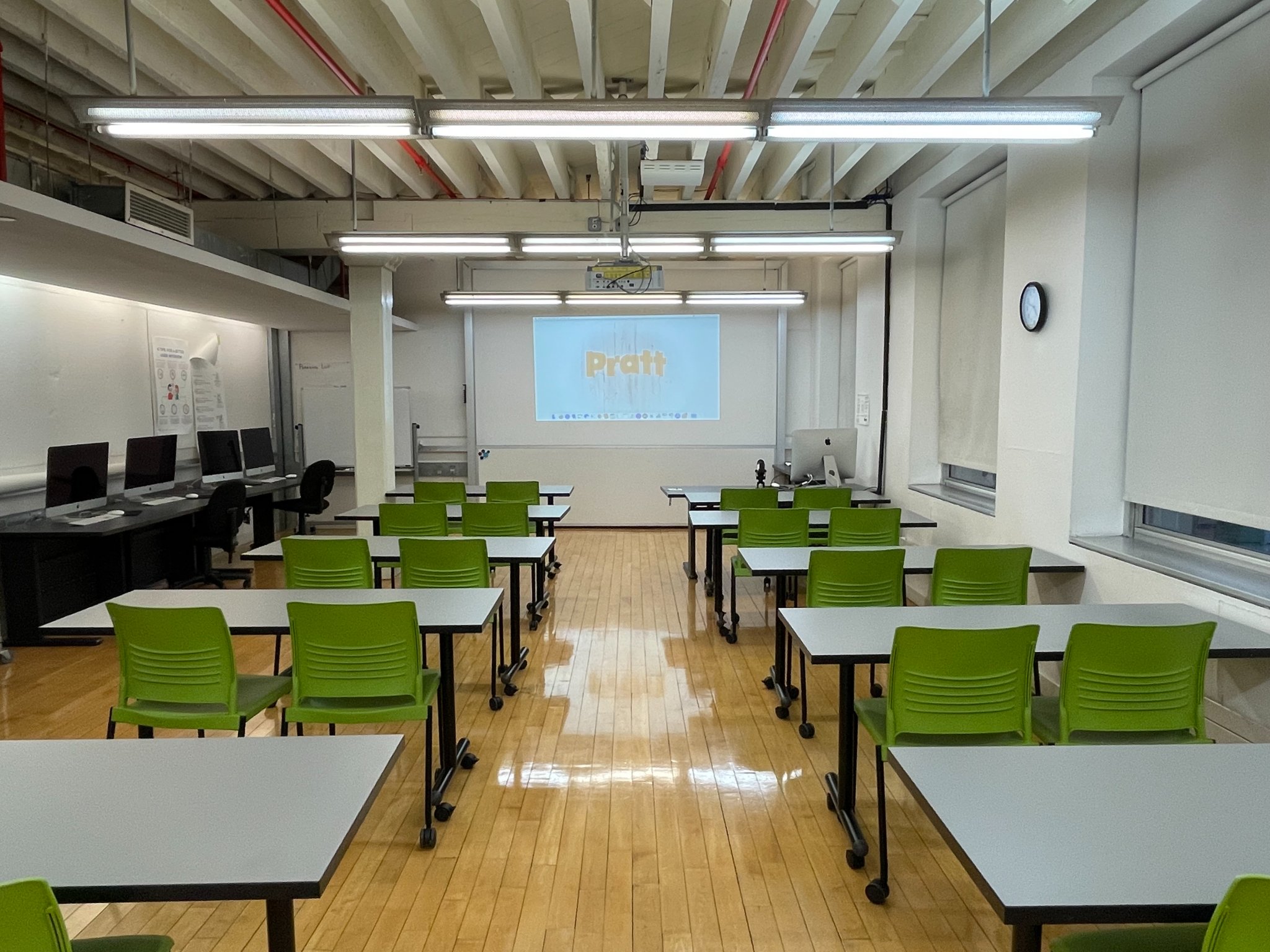 10 work tables each with 2 chairs face a projector screen.
