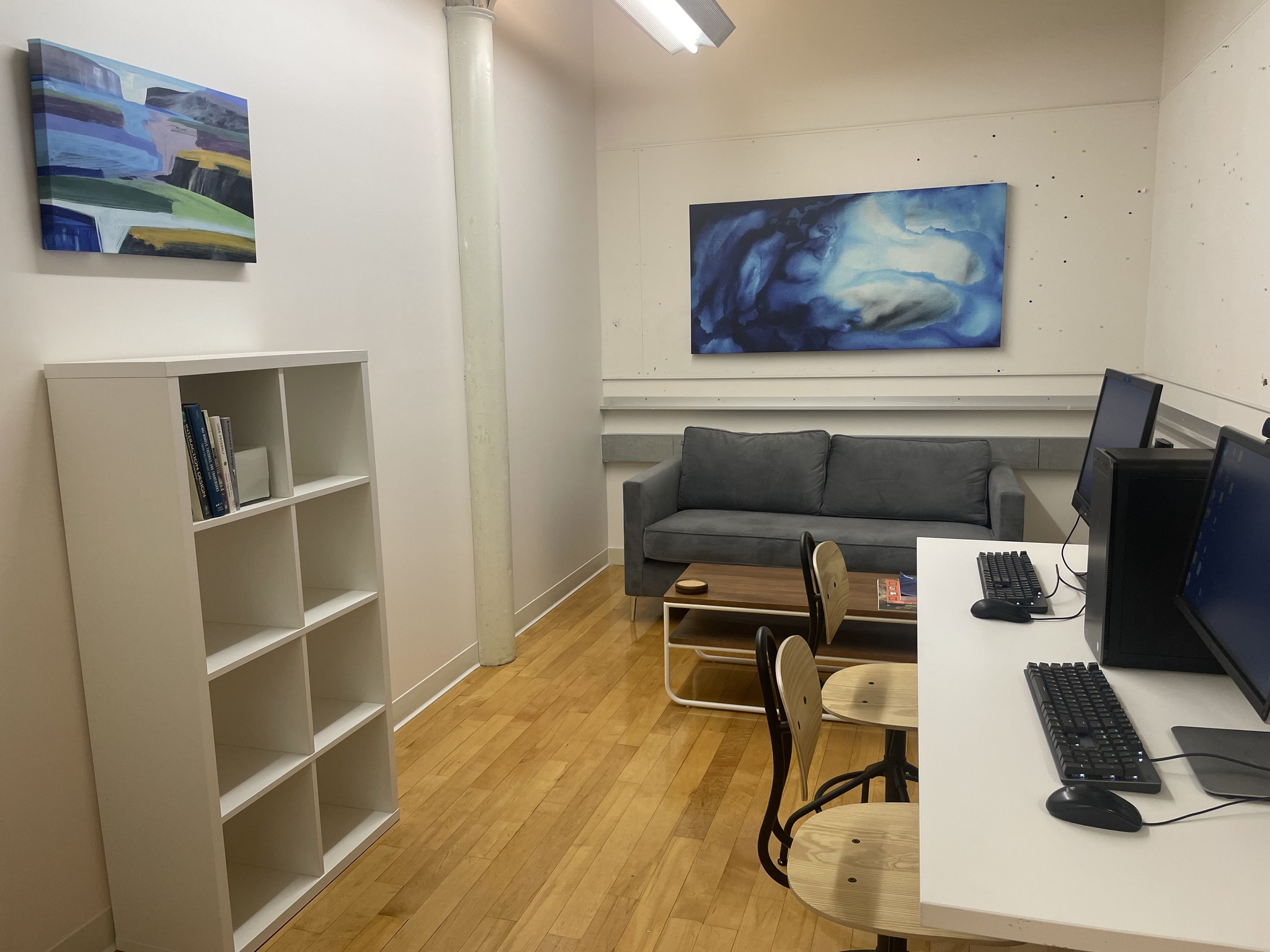 A room with a couch on one wall and two computer workstations at a desk.