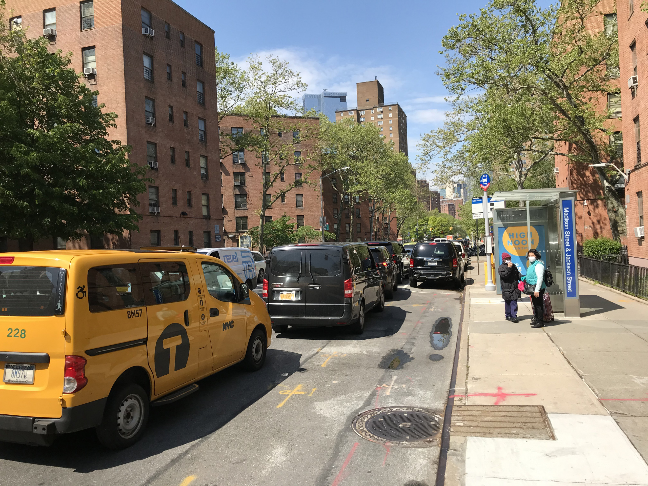 NYC taxis and for-hire vans lined up on a city street between low brick towers