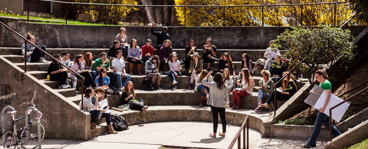 Students sit in an amphitheater as they take notes and raise their hands