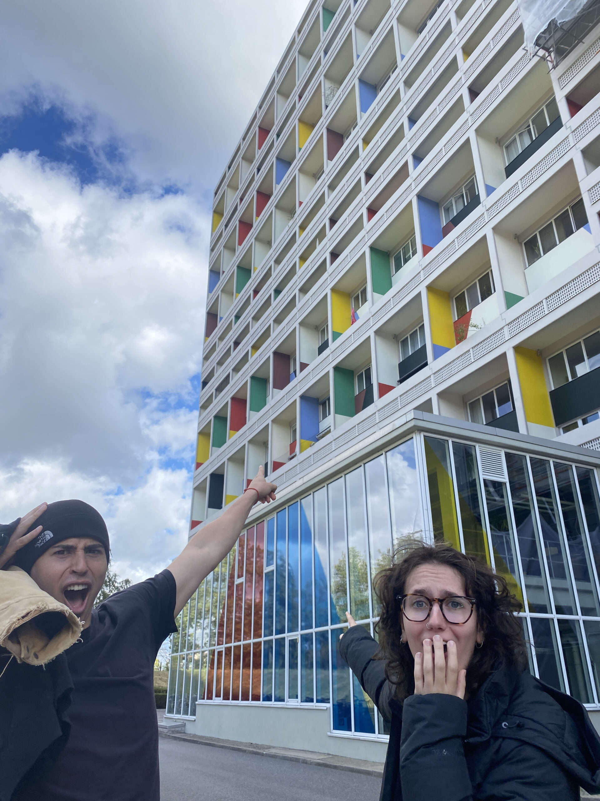 Two students in front of a building in Berlin. They are pointing at the building.