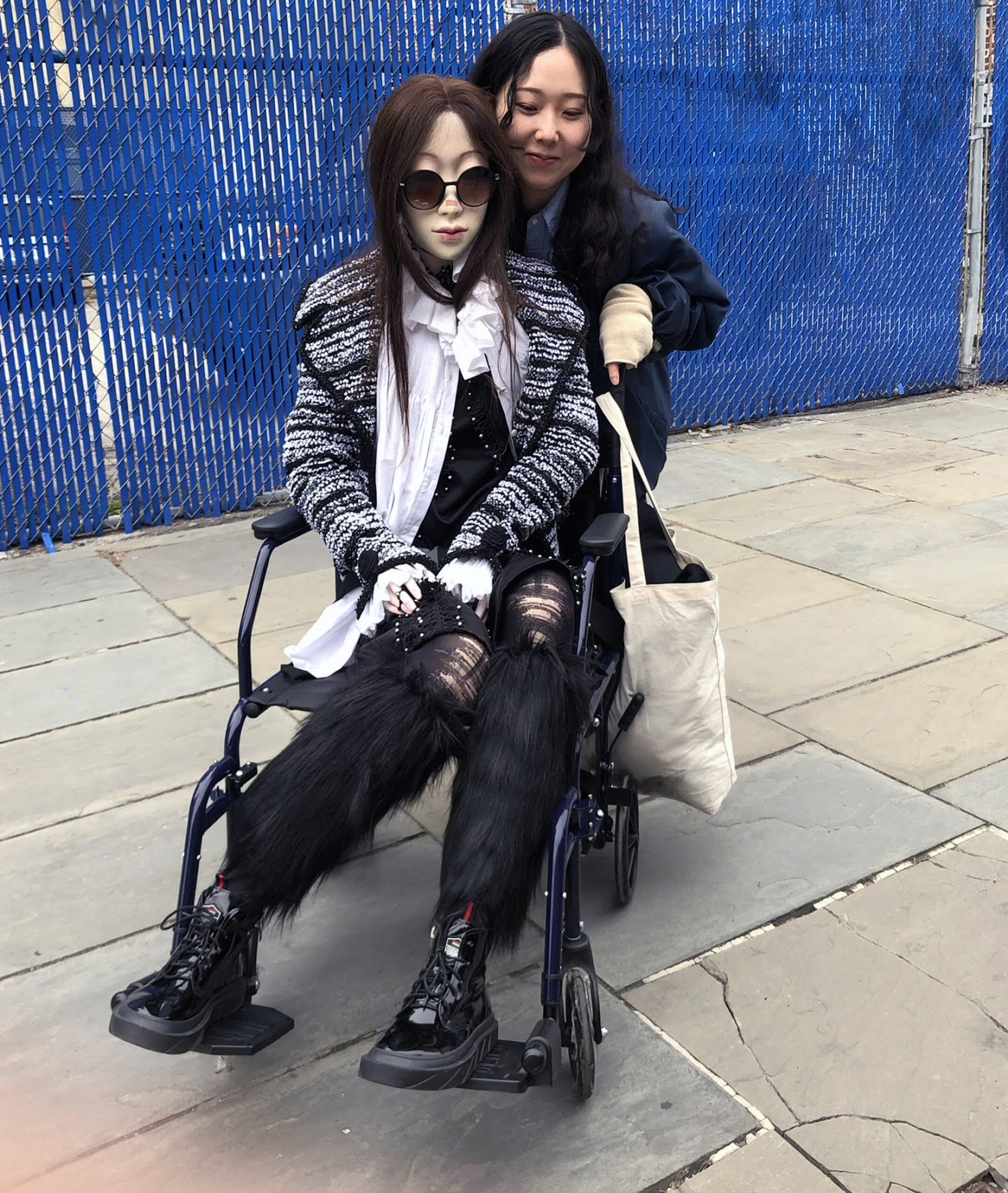 two students, one seated in wheelchair, smiling for a picture, on nyc streets, wearing fashionable autumn clothing