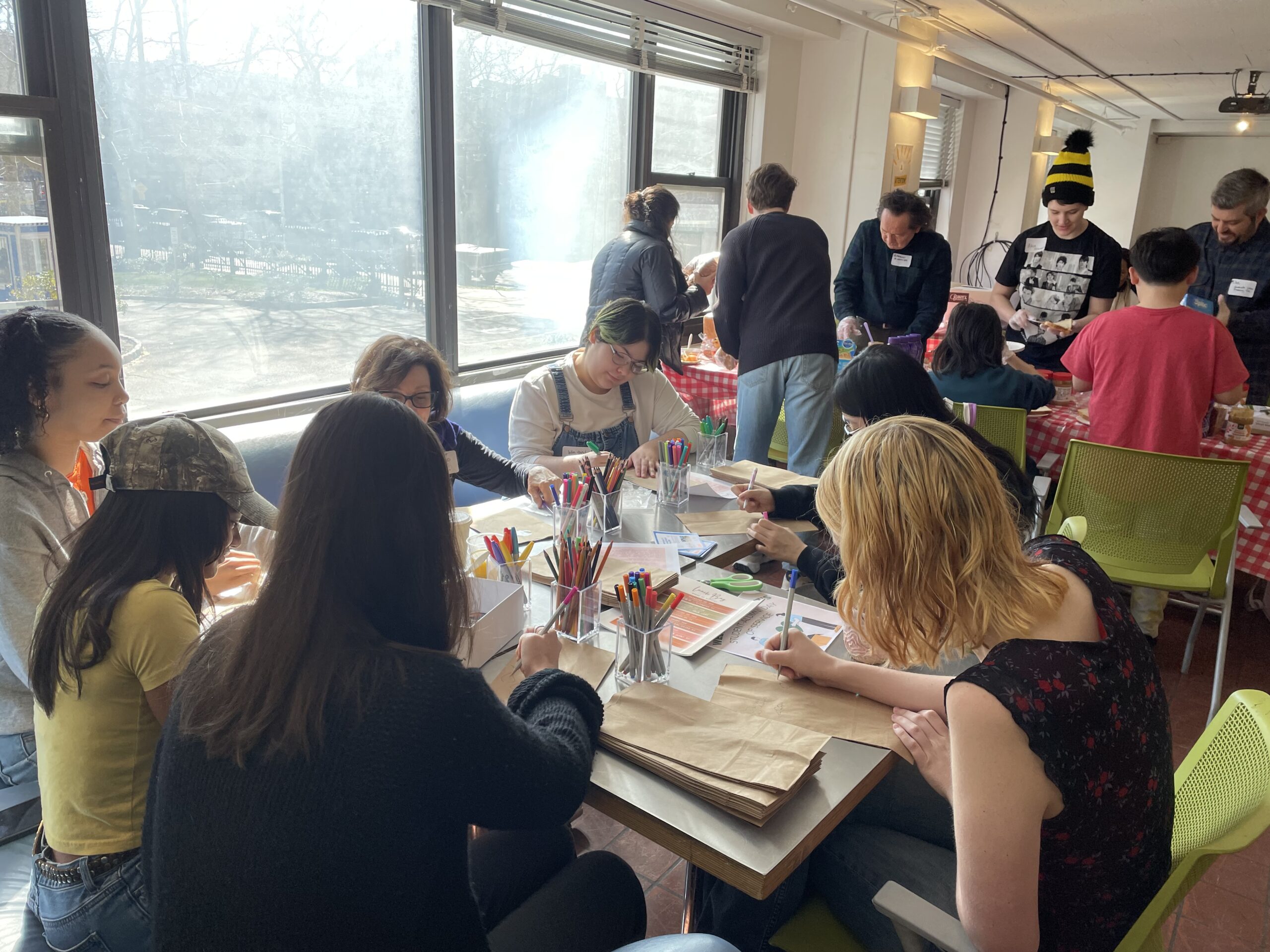 Students gather around tables, drawing and assembling handmade puppet materials during Pratt’s Day of Service for Brooklyn daycare centers.