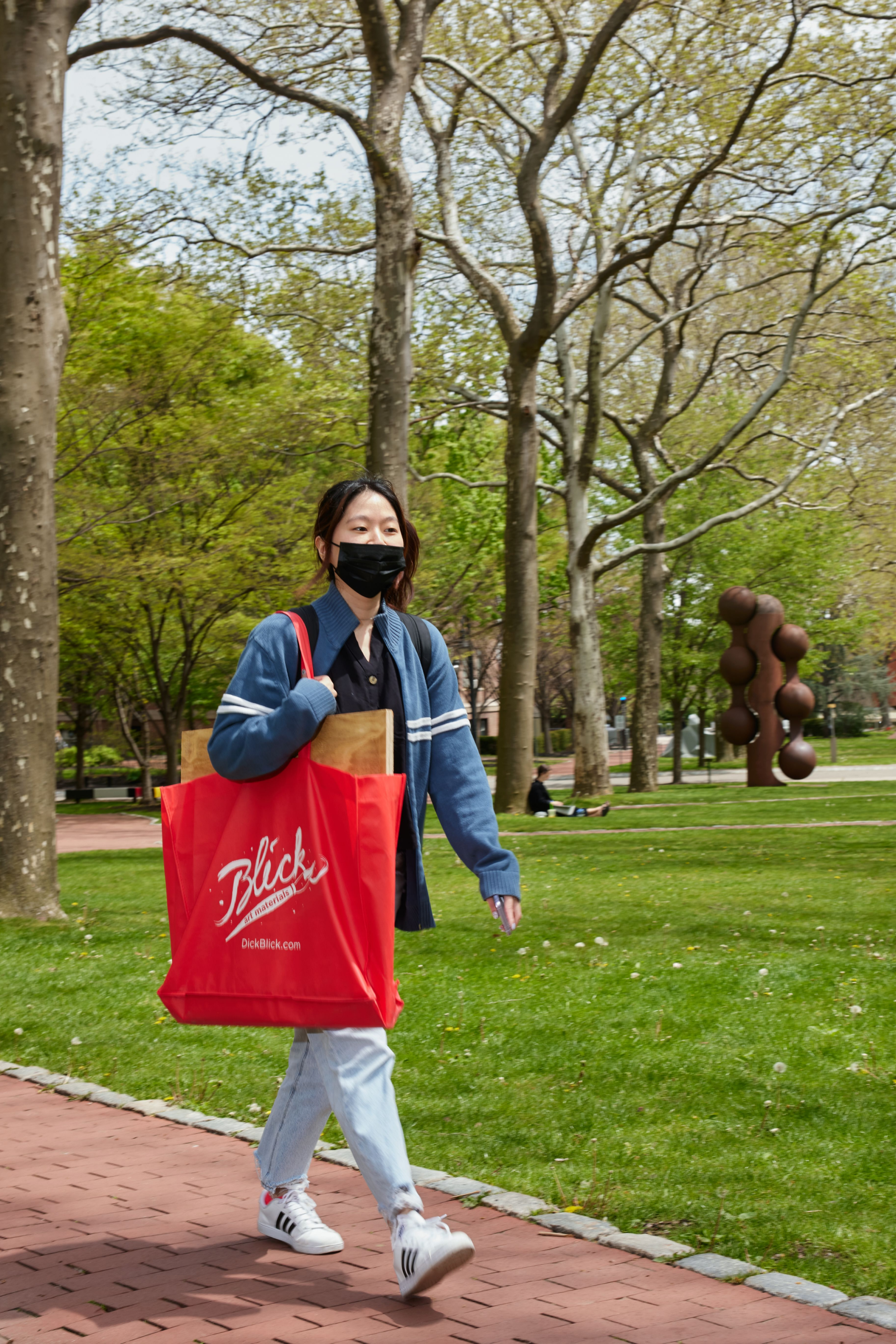 A student walking through campus holding a large red bag
