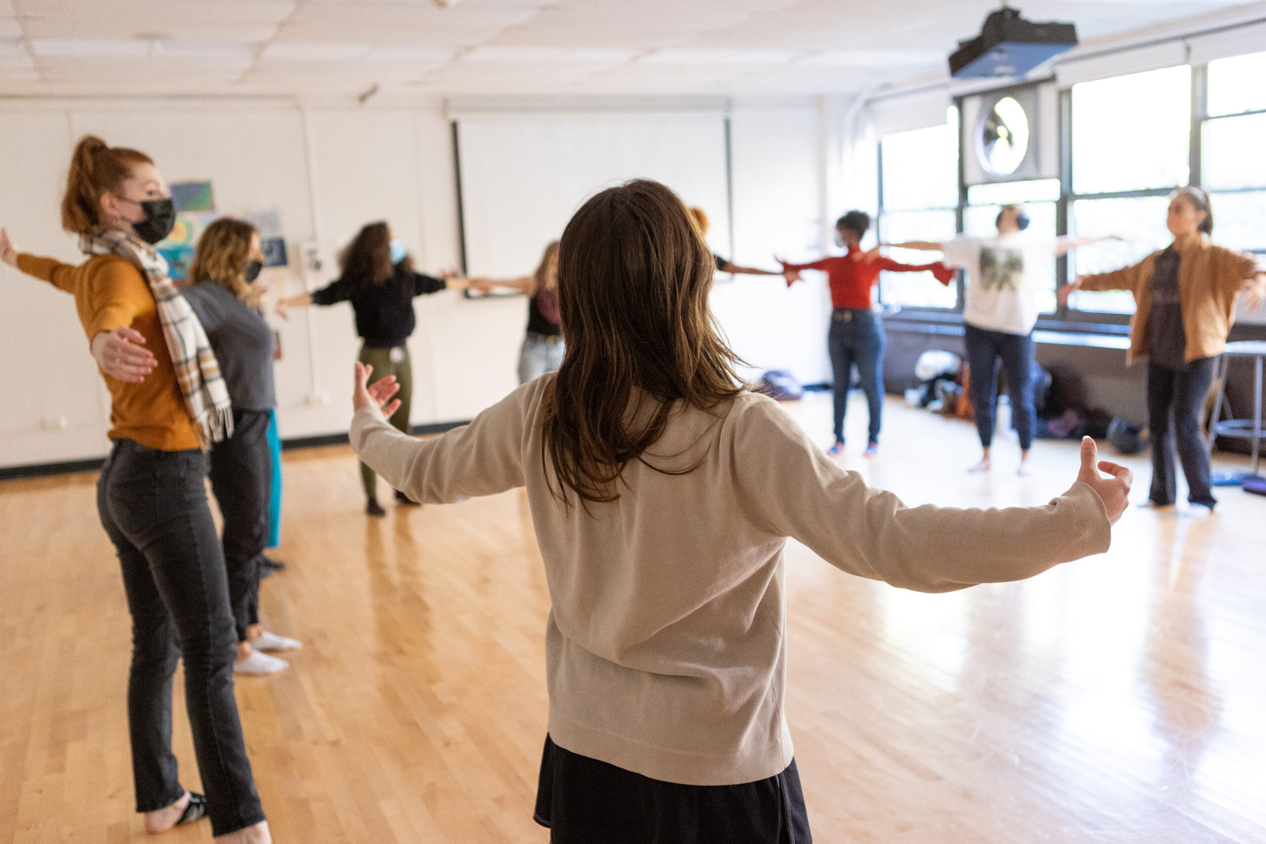 A group of people in a classroom standing in a circle with their arms outstretched.