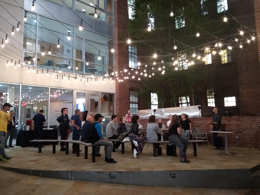 people gathered outside listening to a talk by the artist who created the light string art work