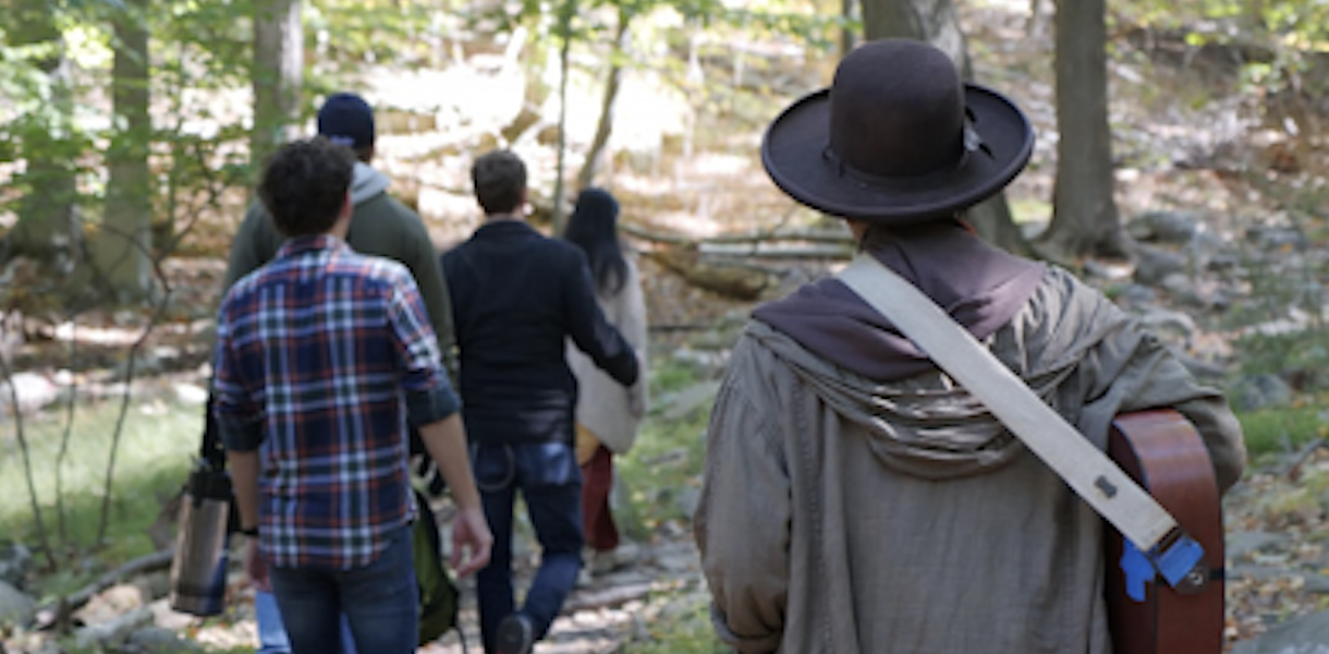picture of actors walking through the woods playing instruments