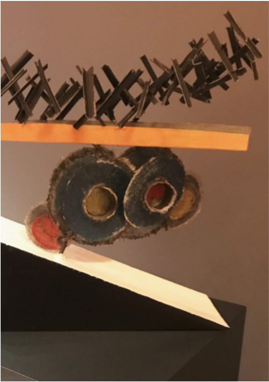 sculpture consisting of metal plates with holes in middle, sitting on a slanted board, with metal string above the plates