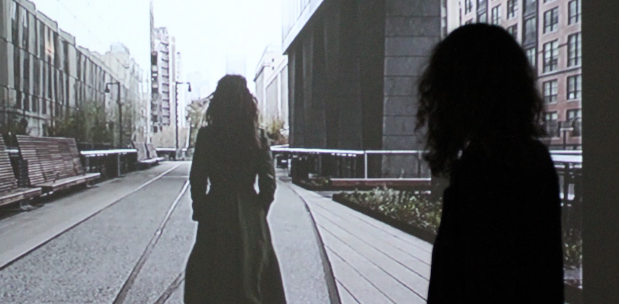 film projector depiction of woman walking on NYC highline pedway, with woman watching projectioj