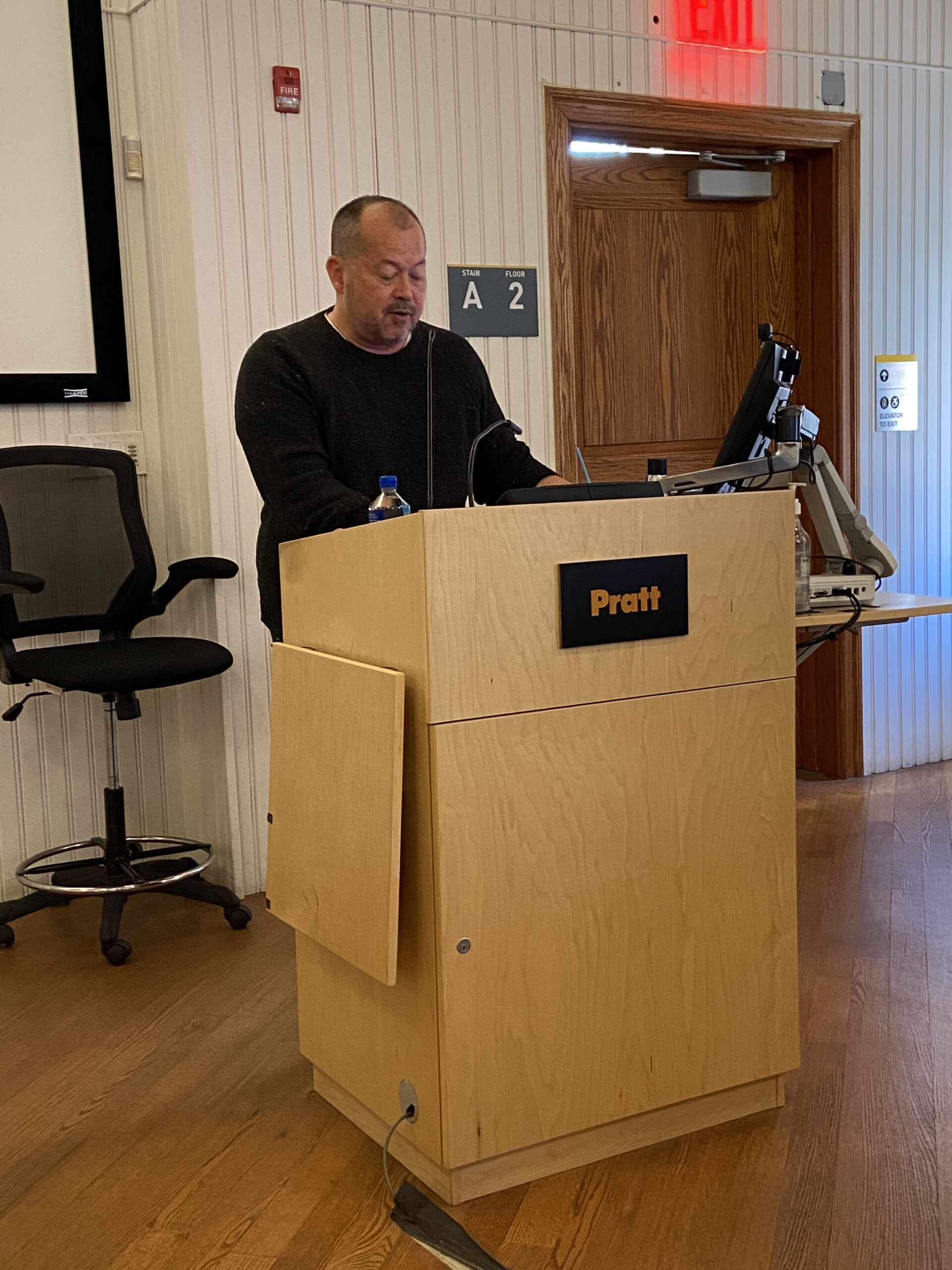 A man stands behind a wooden podium labeled