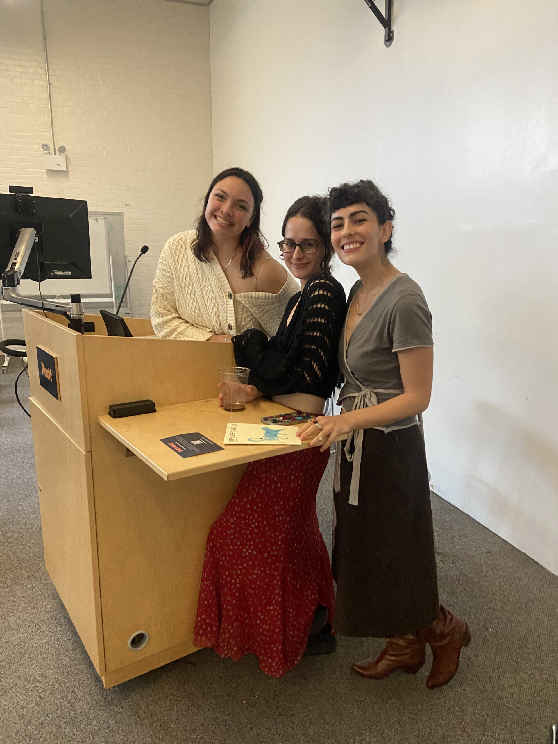Three women smile and pose together behind a wooden podium labeled