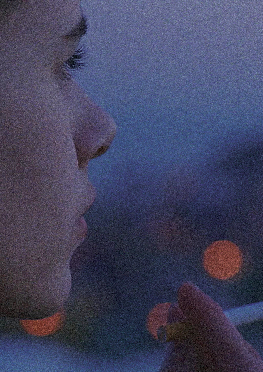 Close-up on the face of a young person looking out into dusk with lights in the distance