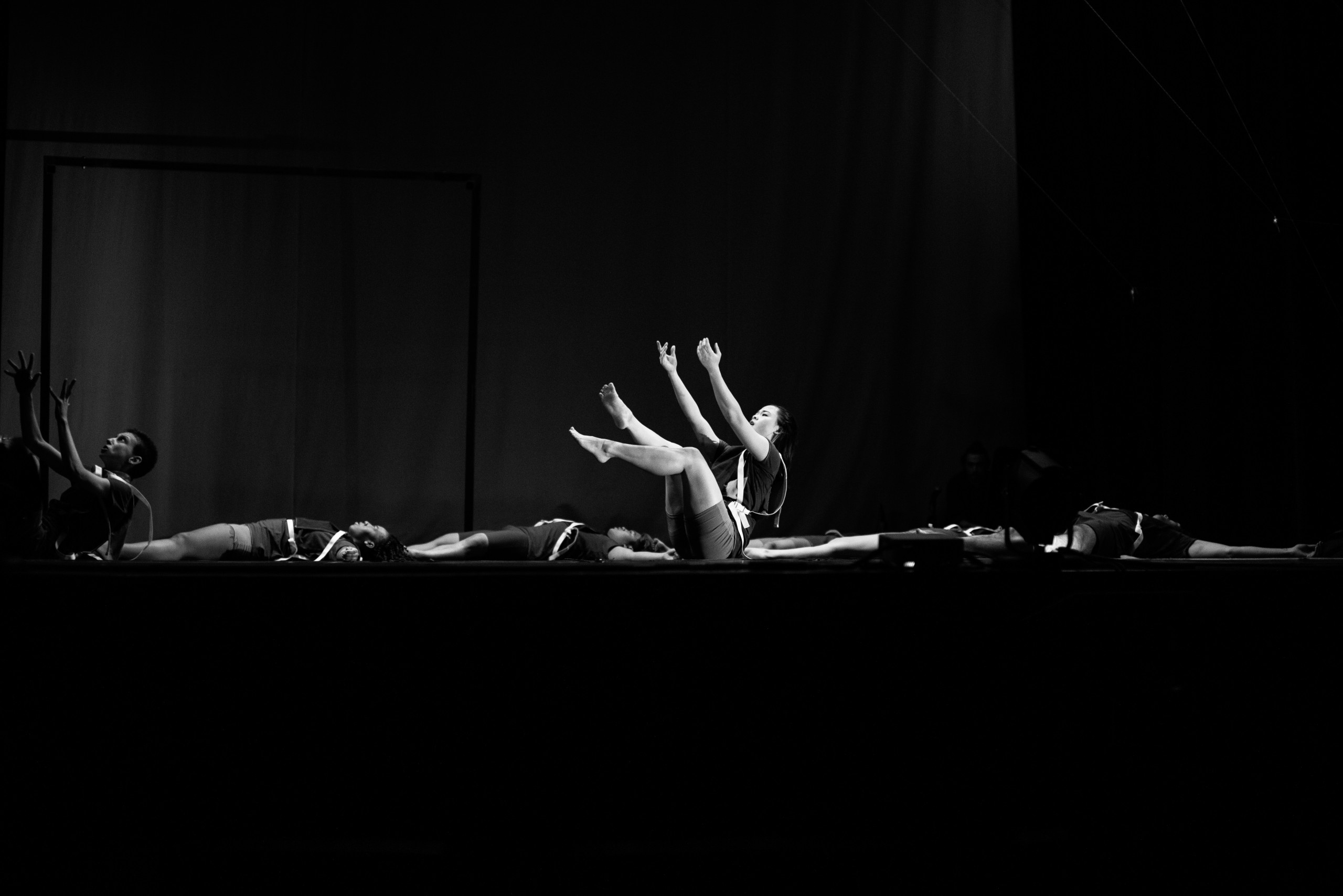 A dancer reaches up from a seated position on a stagge