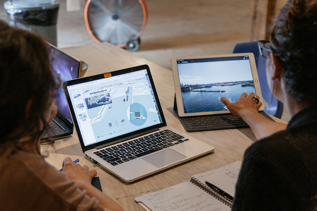 Picture of two individuals working on a project with a laptop on their left and a tablet on their right