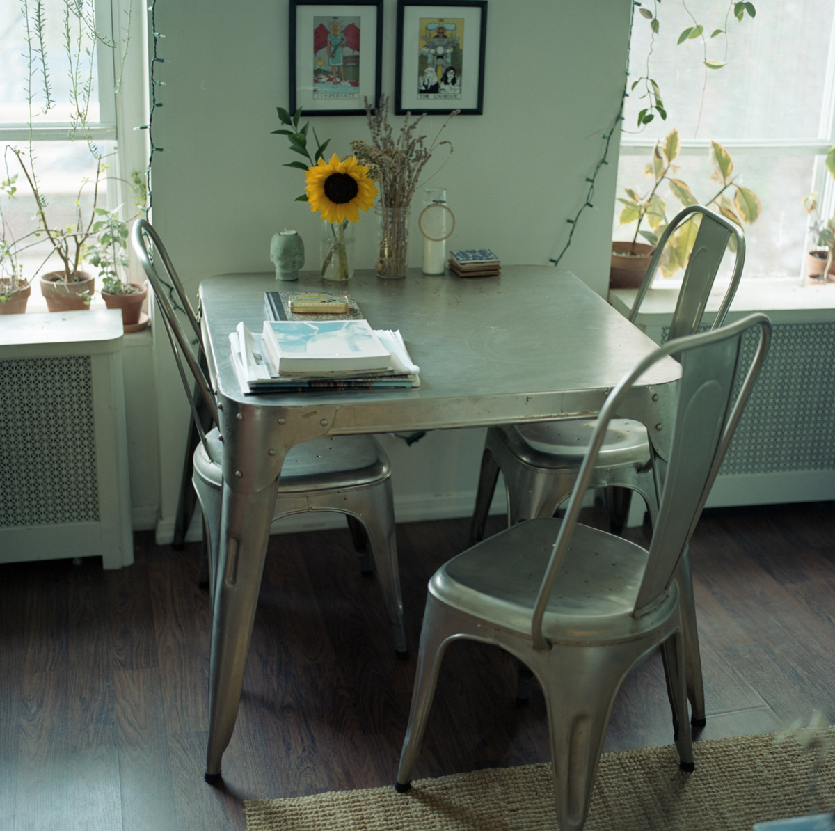 Picture of a table with three chairs, a sunflower and books on top.